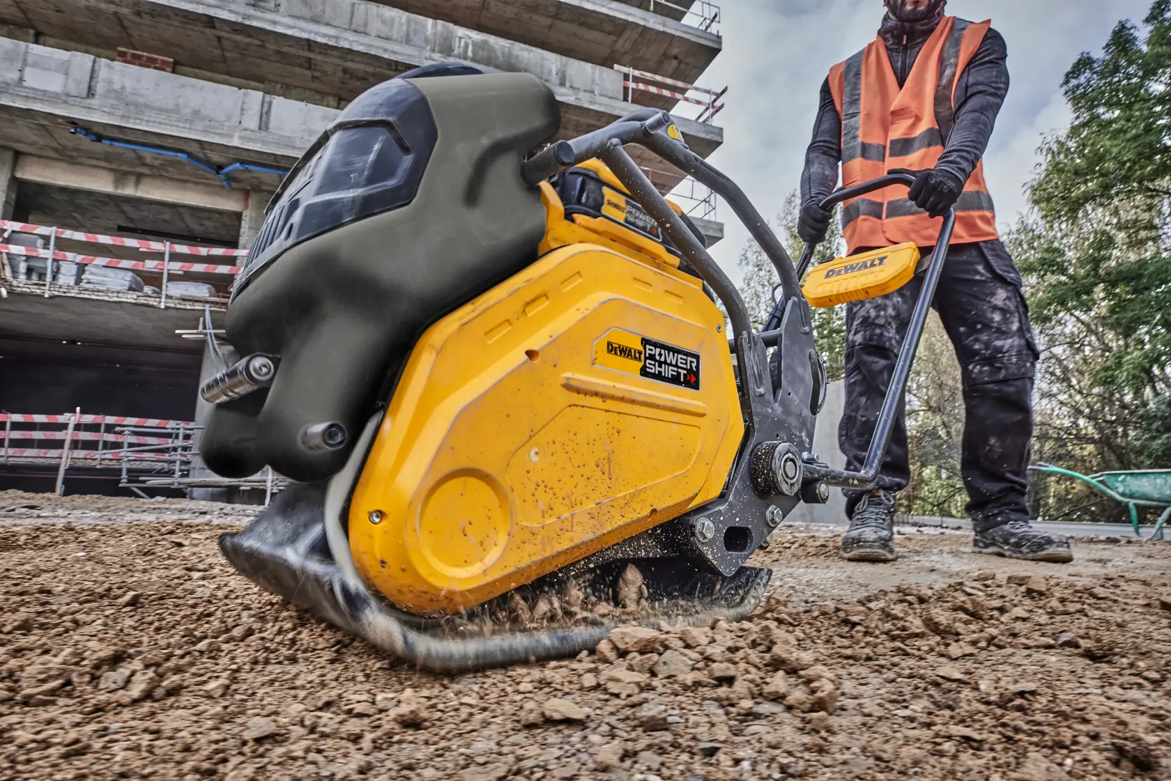 DEWALT Power Shift plate compactor in use on soil at a construction site by worker in orange vest.
