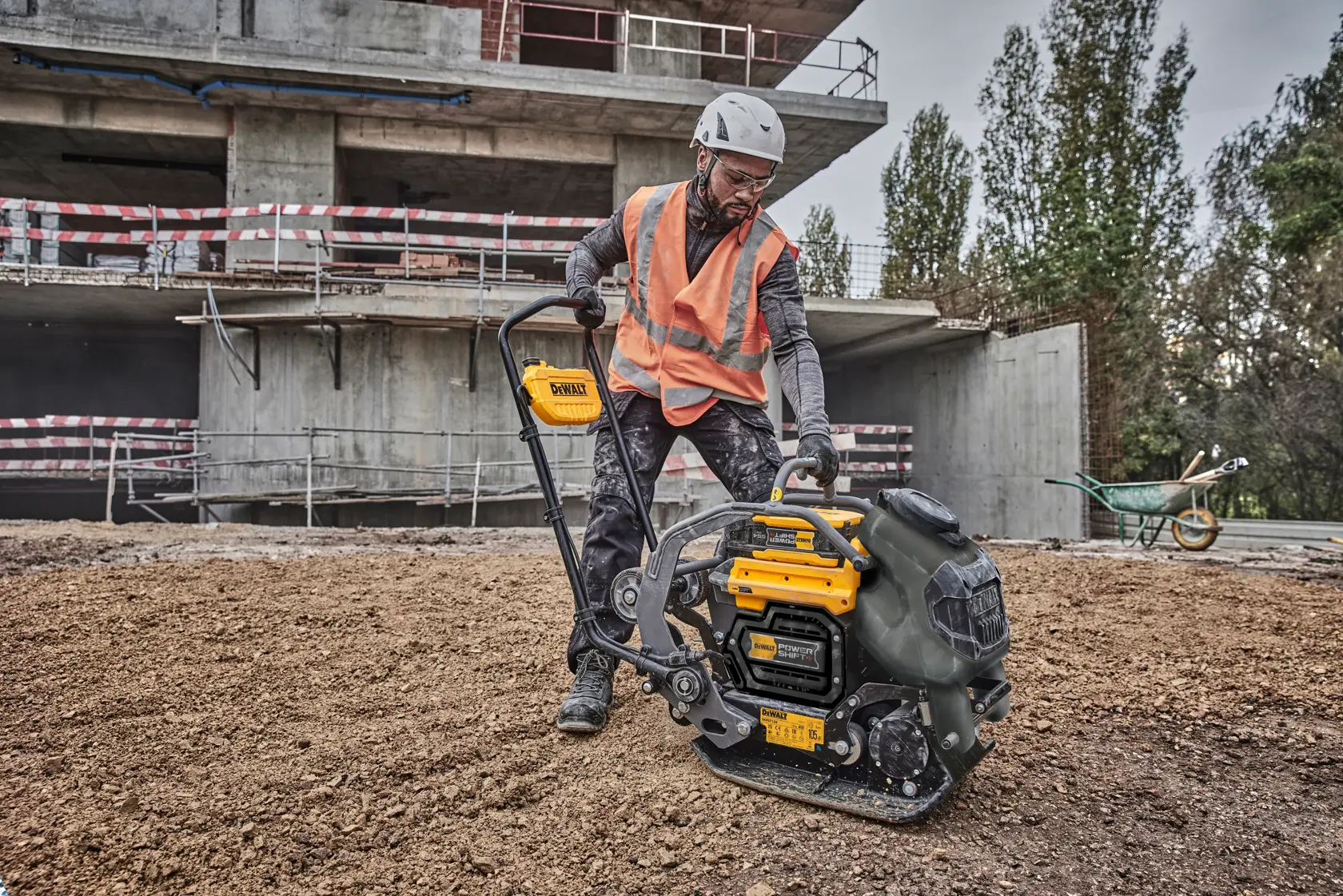 Worker with DEWALT plate compactor DCPS7154N on construction site, wearing safety gear and orange vest.