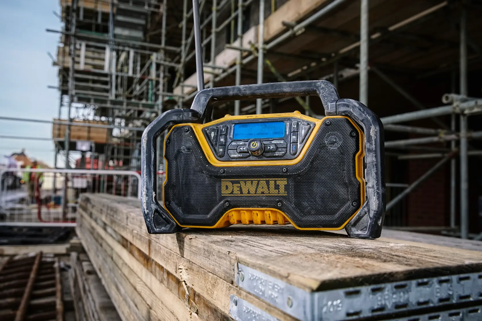 DEWALT jobsite radio on wooden planks at a construction site, surrounded by scaffolding and building materials.