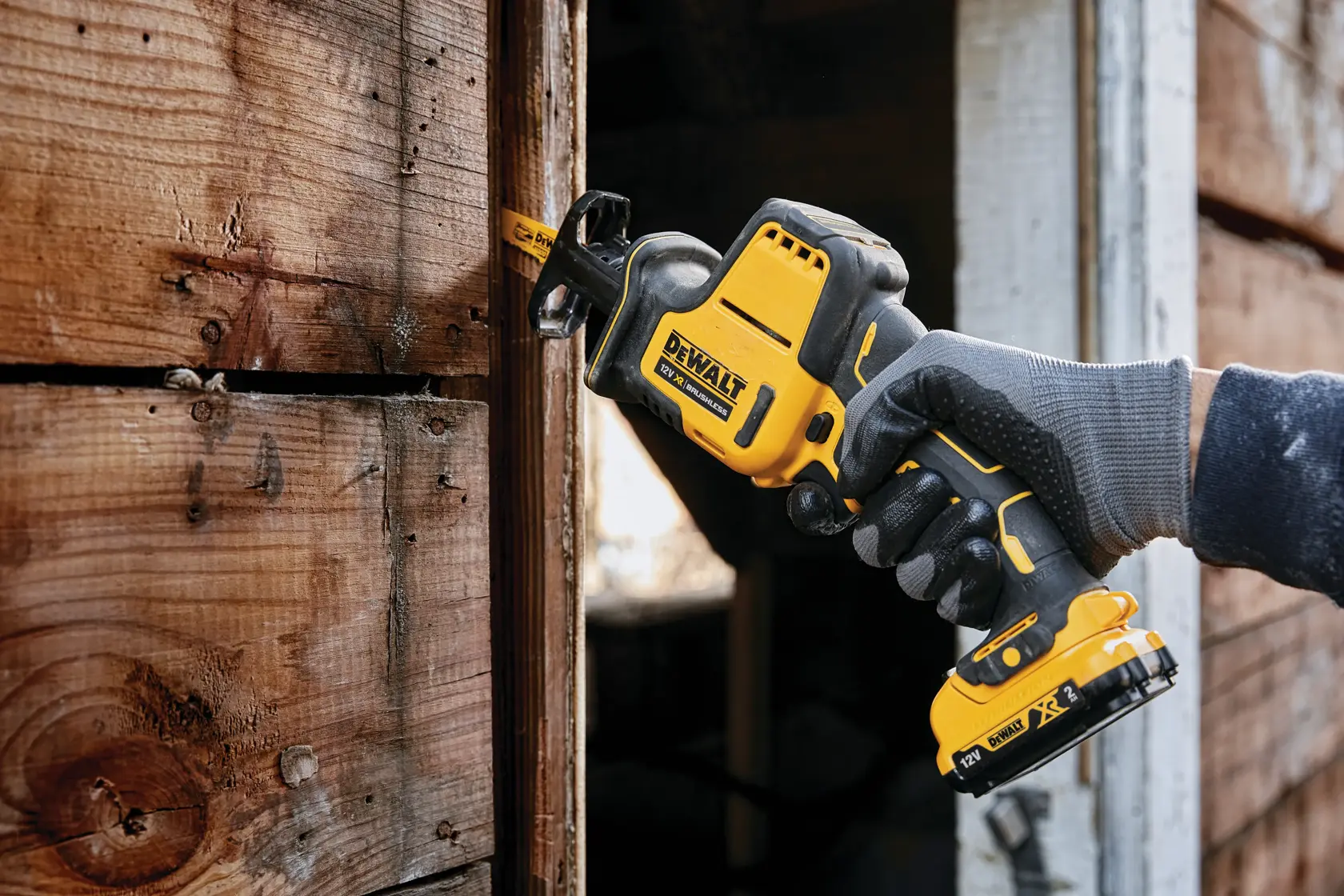 DEWALT cordless reciprocating saw cutting wood, held by gloved hand during outdoor carpentry work.