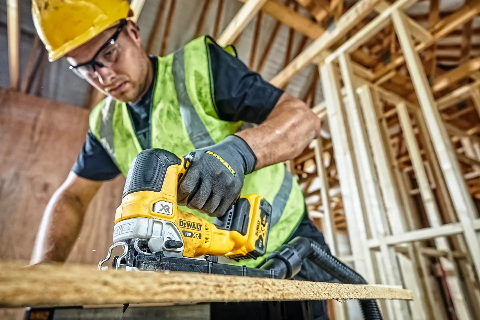 Worker using a DEWALT DCS334N jigsaw on wood at a construction site, wearing safety gear and gloves.