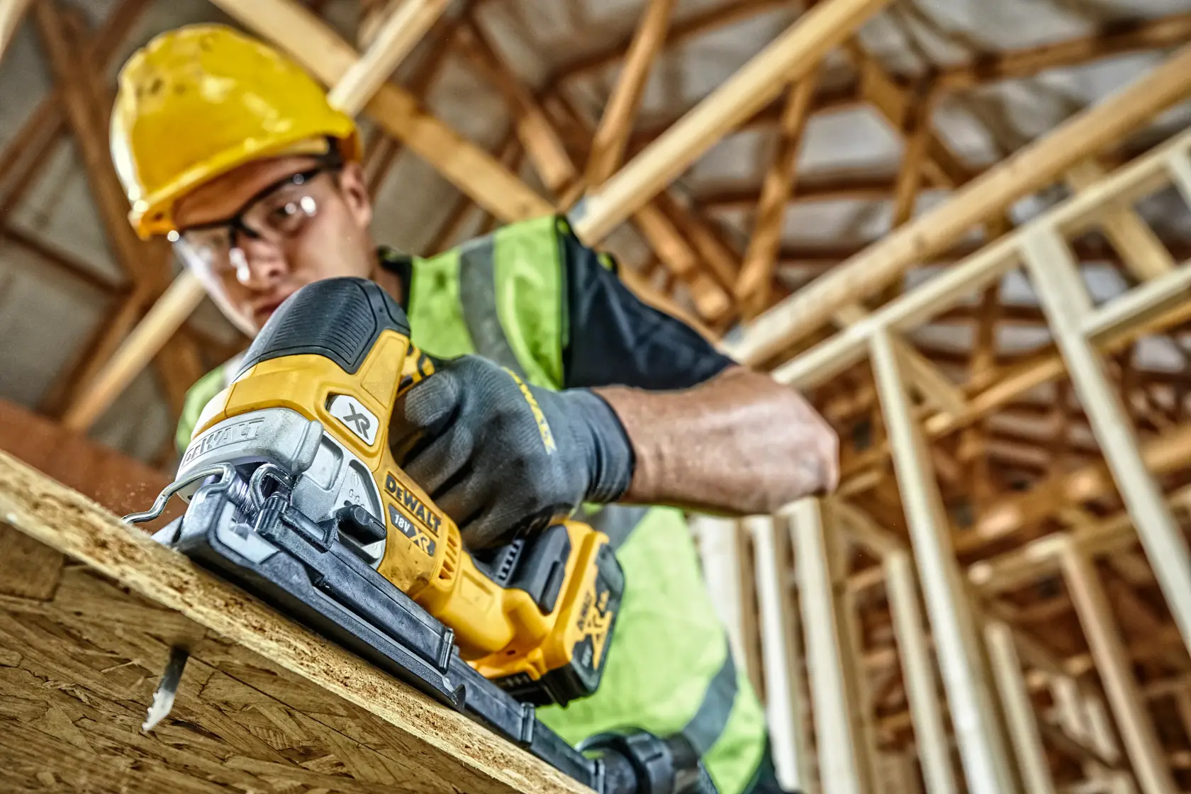 DEWALT cordless jigsaw cutting wood at a construction site, held by a worker in safety gear.