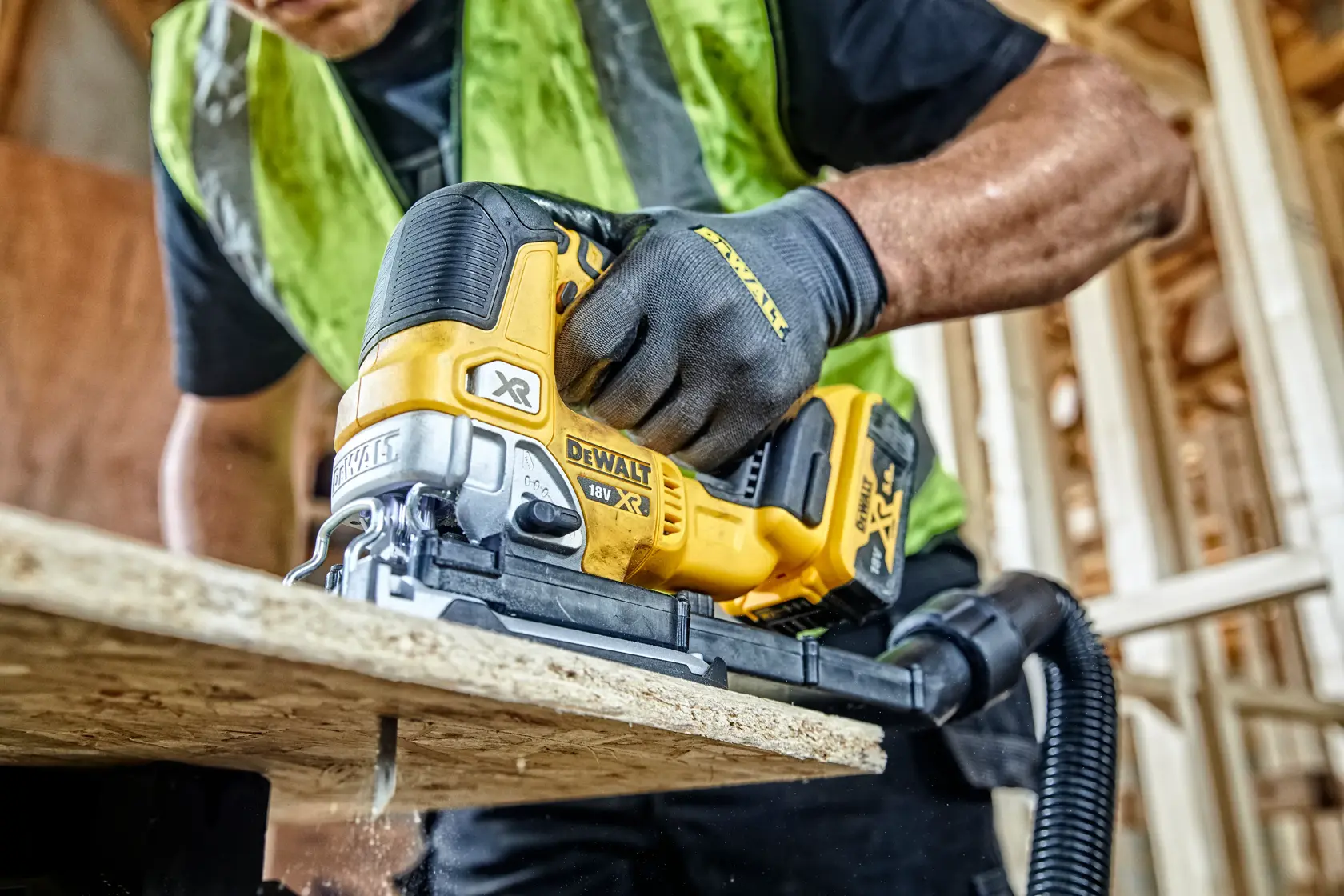 DEWALT cordless jigsaw cutting wood, operated by person wearing gloves and safety vest at construction site.