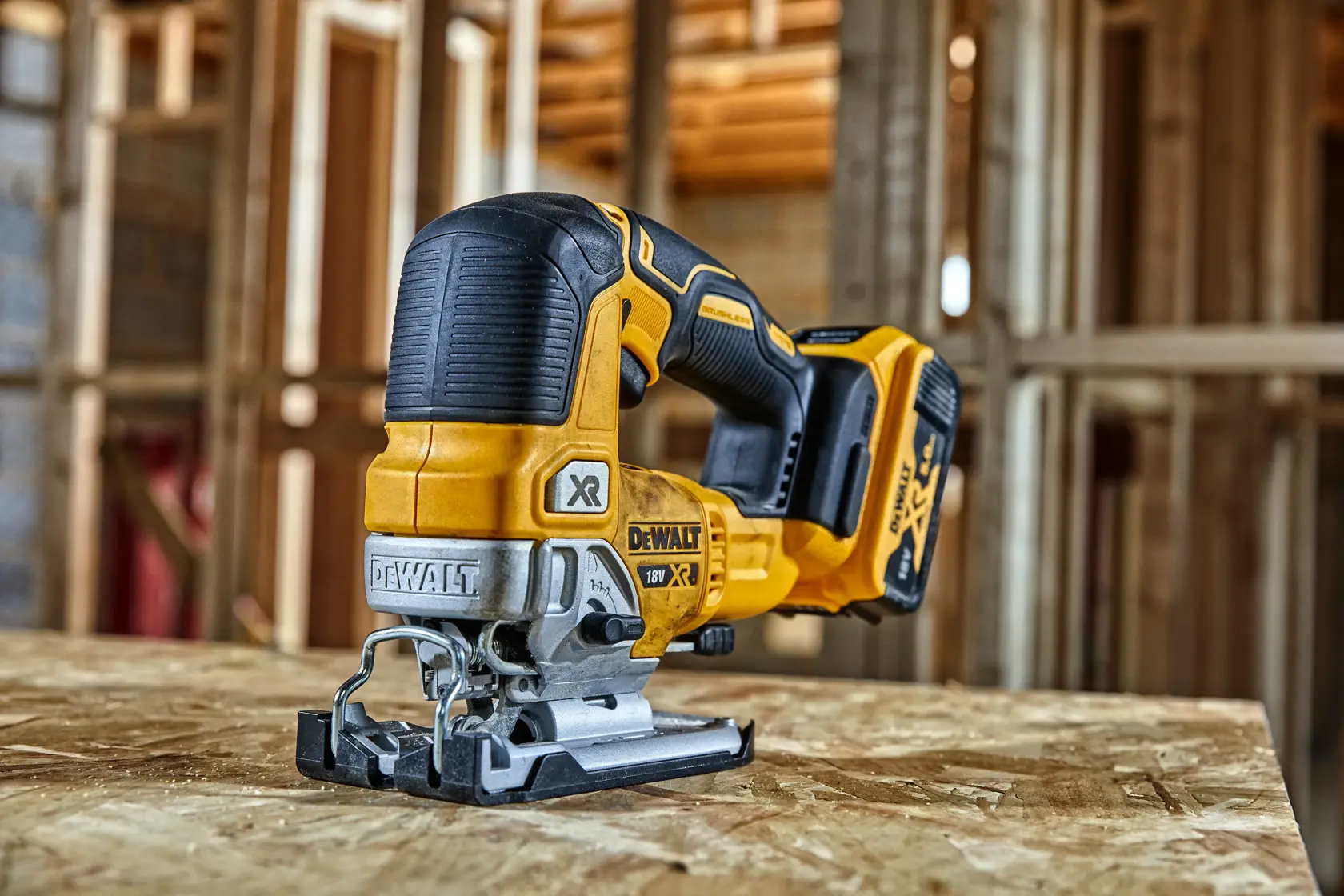 DEWALT cordless jigsaw placed on plywood in a construction site with wood framing visible in the background.