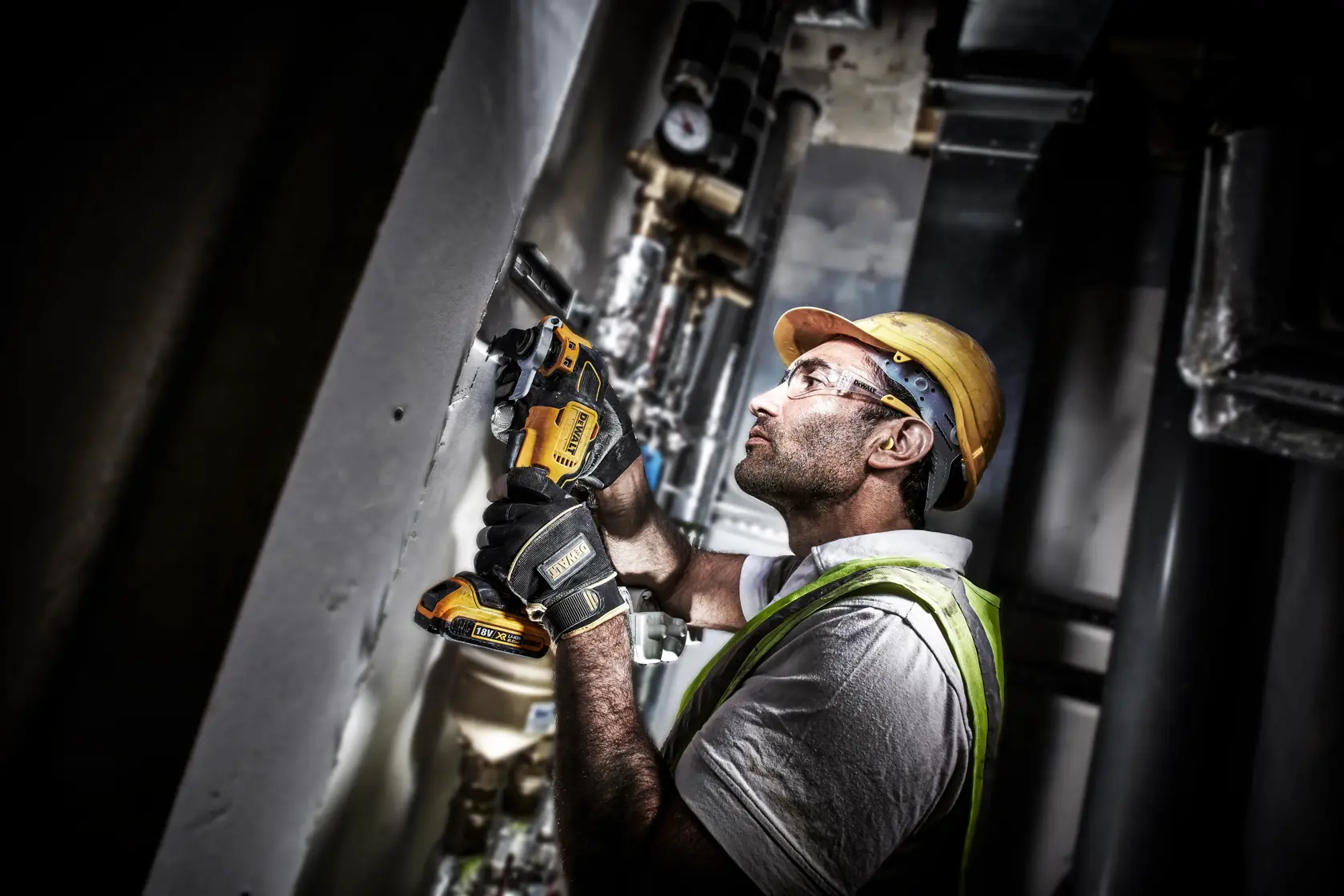 Worker uses DEWALT DCS356N cordless tool on wall, wearing gloves, helmet, and safety vest at an industrial site.