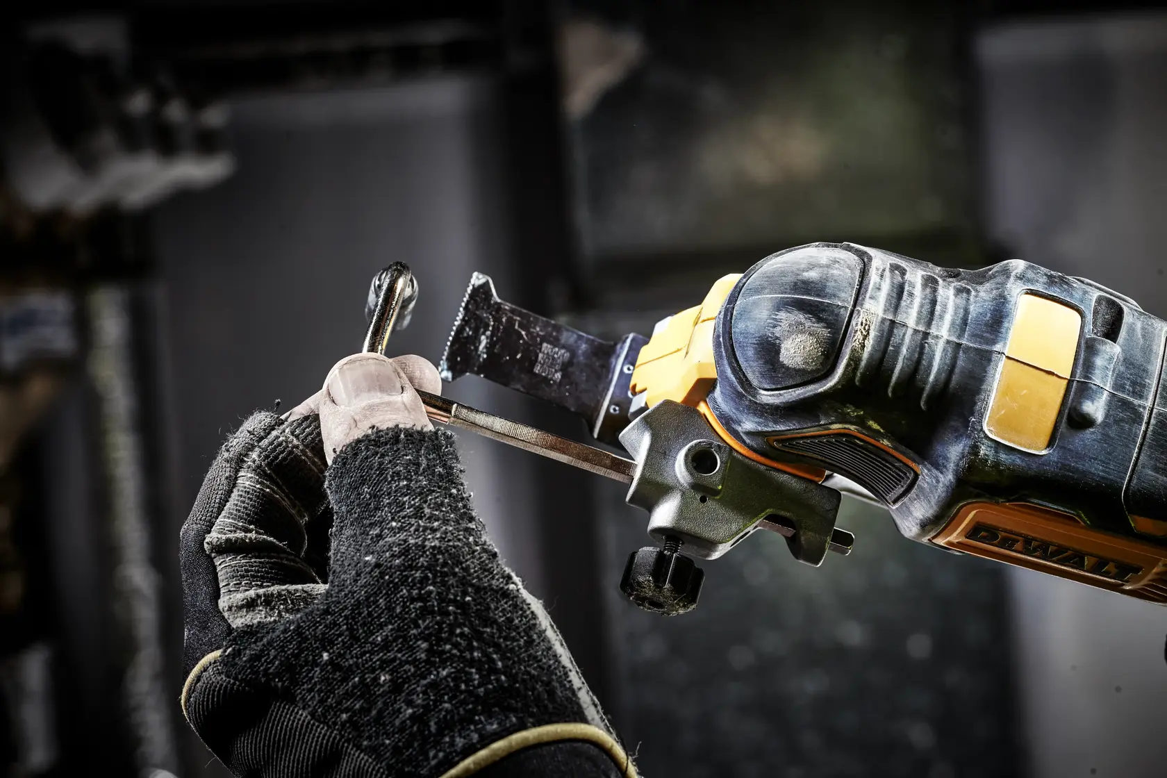 Person uses a DEWALT oscillating tool to cut metal, wearing protective gloves for safety.