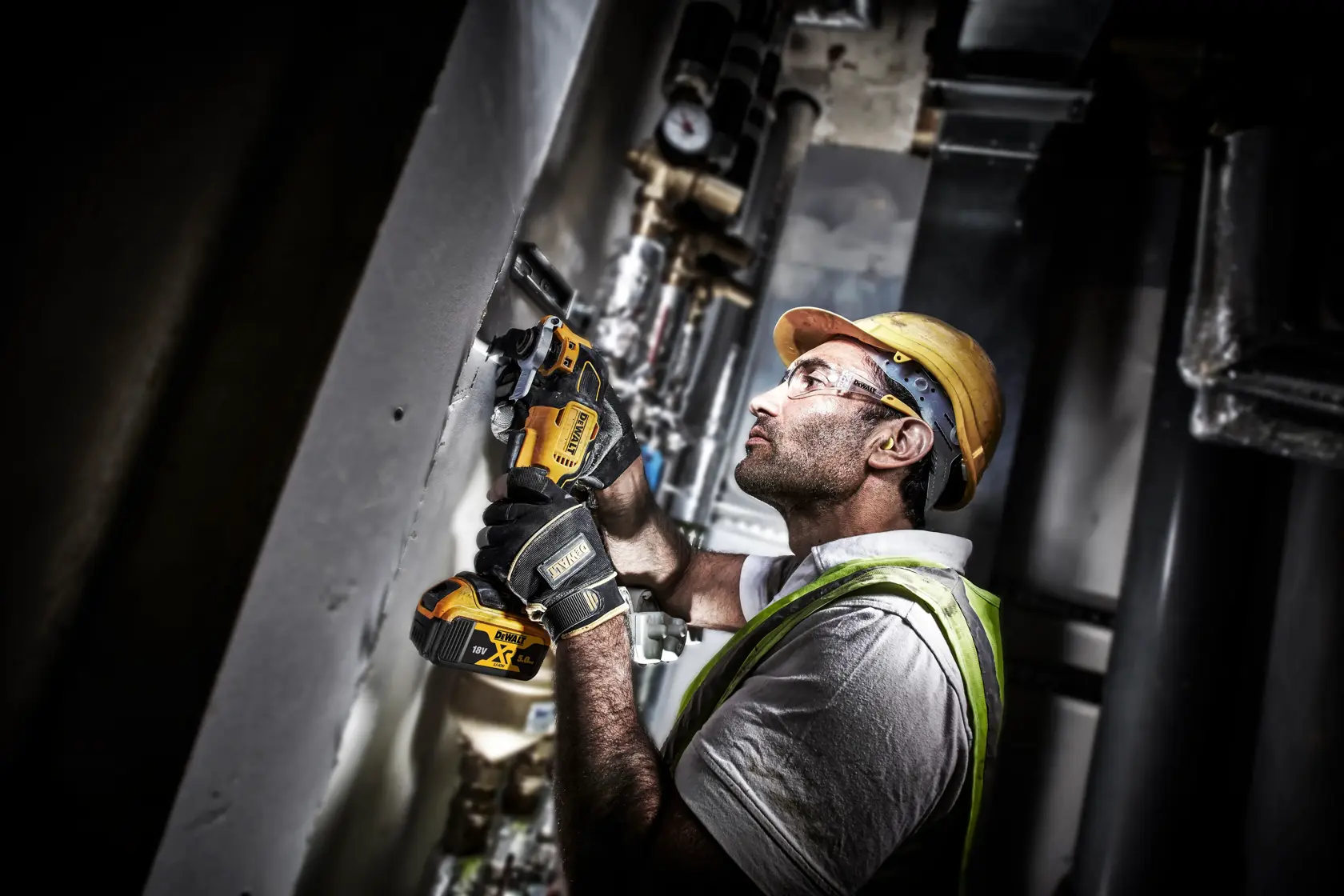 Worker using a DEWALT DCS356P2 cordless multi-tool to cut wall material inside an industrial setting.
