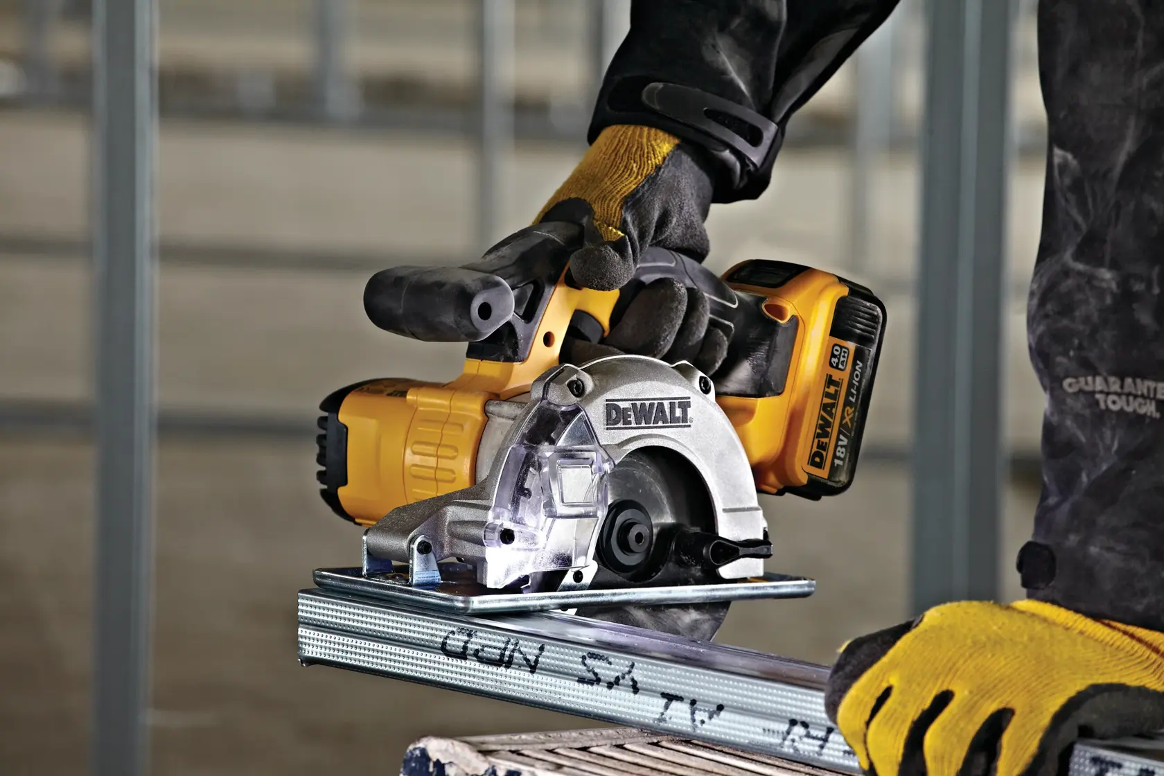 DEWALT cordless metal cutting saw in use, worker wearing gloves and safety gear, cutting steel profile indoors.