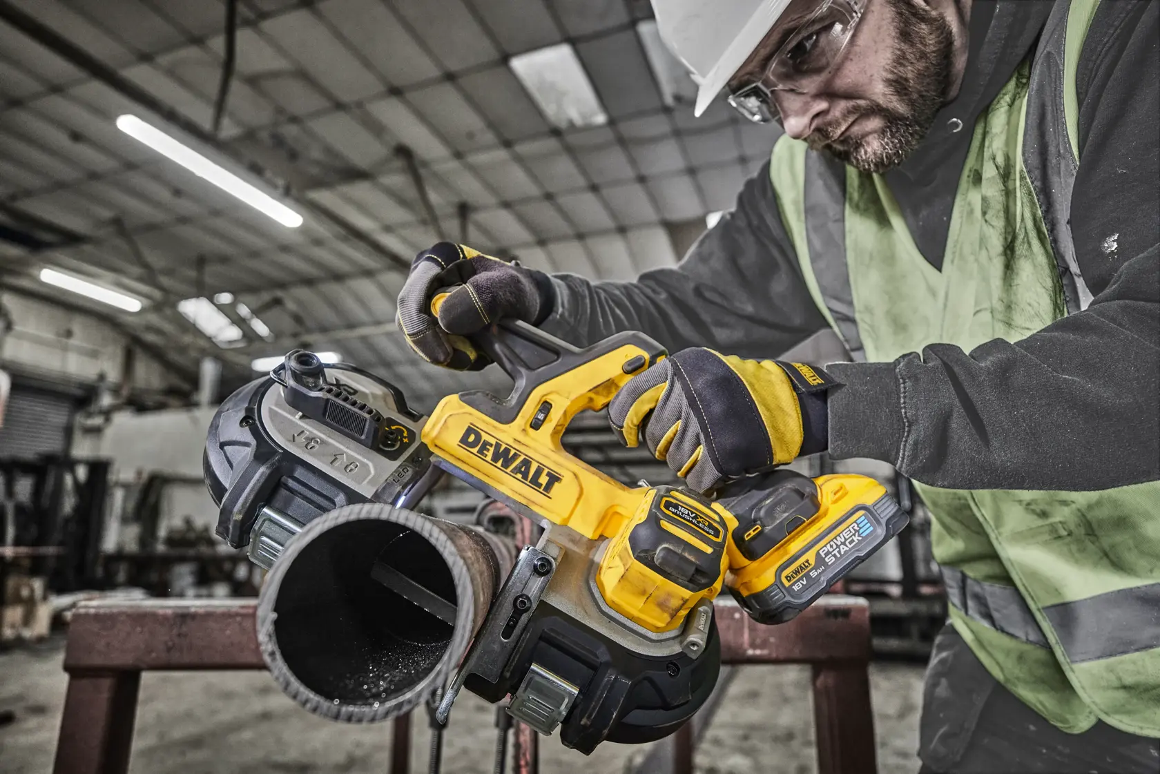 DEWALT cordless band saw cutting a metal pipe in an industrial workshop setting with gloved operator.