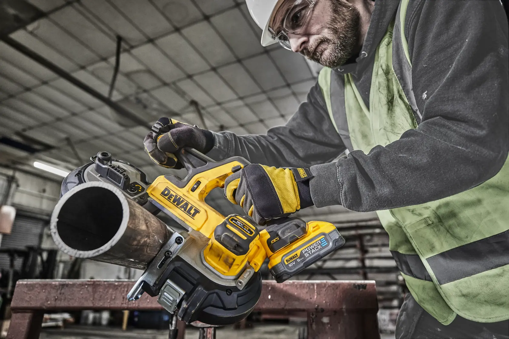 Worker uses DEWALT DCS378N cordless band saw to cut a metal pipe in an industrial setting.