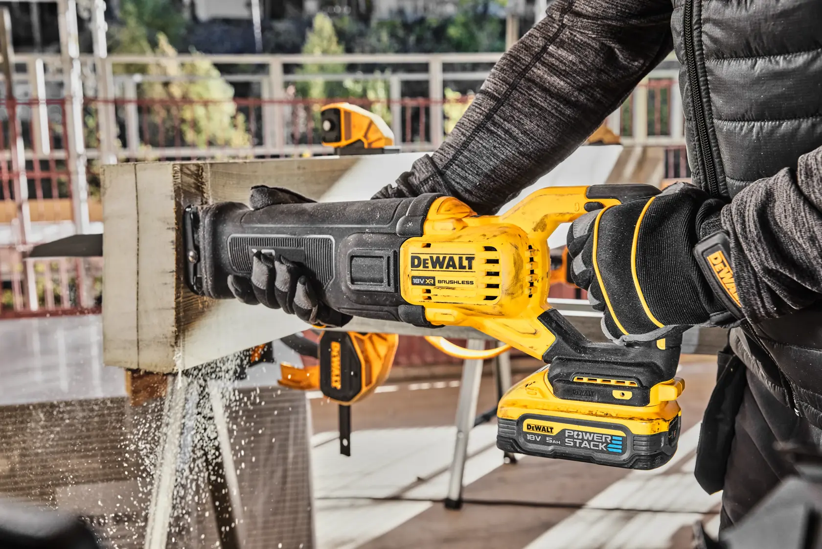 En person bruker en DEWALT batteridrevet bajonettsag til å kutte gjennom en trebjelke, mens sagflis flyr. Sagen har et DEWALT POWERSTACK-batteri, og scenen er på en arbeidsplass.