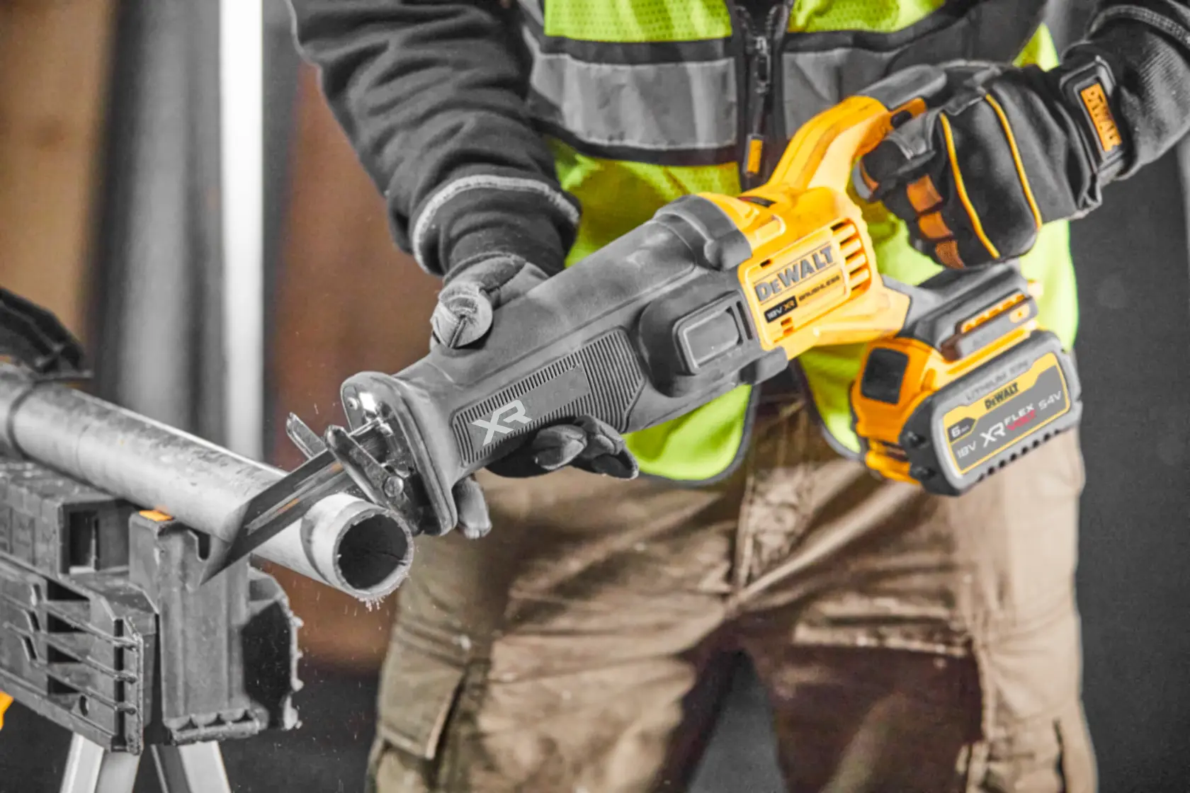 DEWALT cordless reciprocating saw cutting a metal pipe, held by a worker wearing gloves and safety vest.