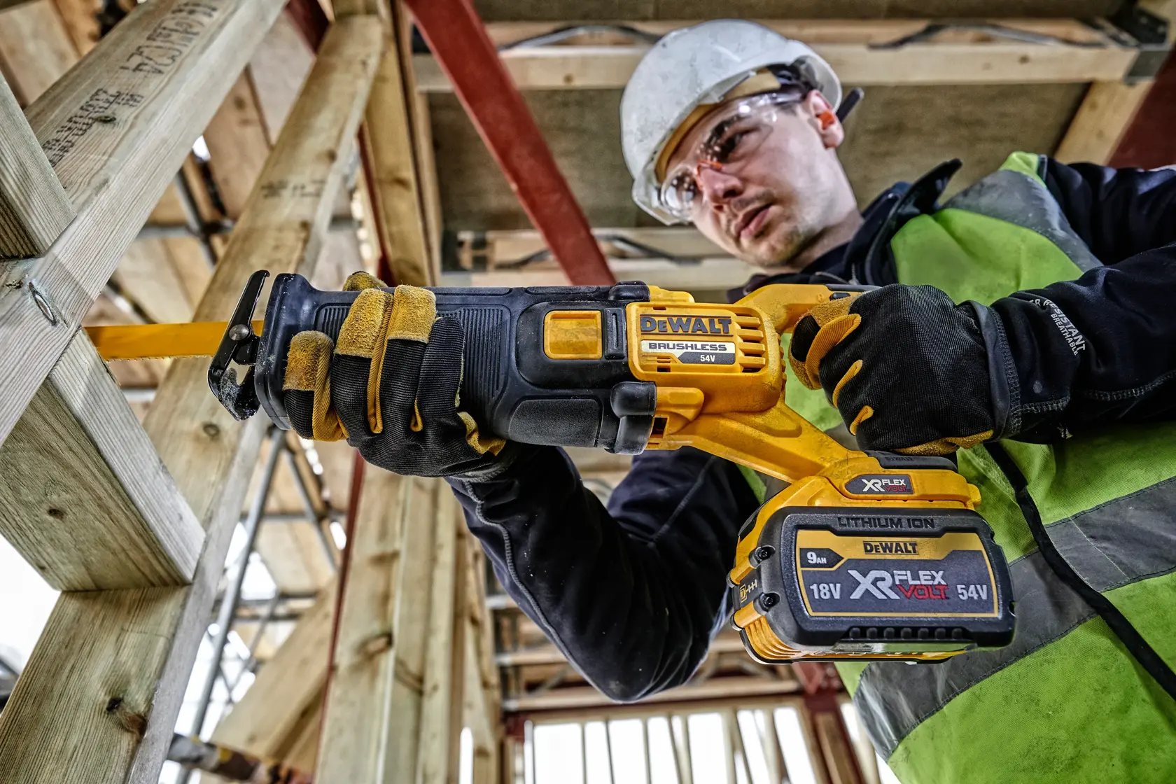Worker using a DEWALT DCS389N cordless reciprocating saw on wood at a construction site.
