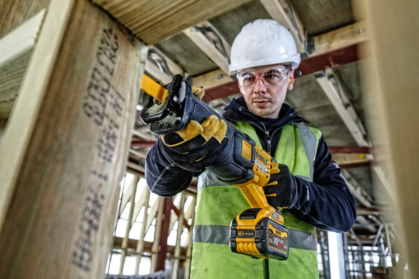 Worker using a DEWALT cordless reciprocating saw to cut wood at a construction site.