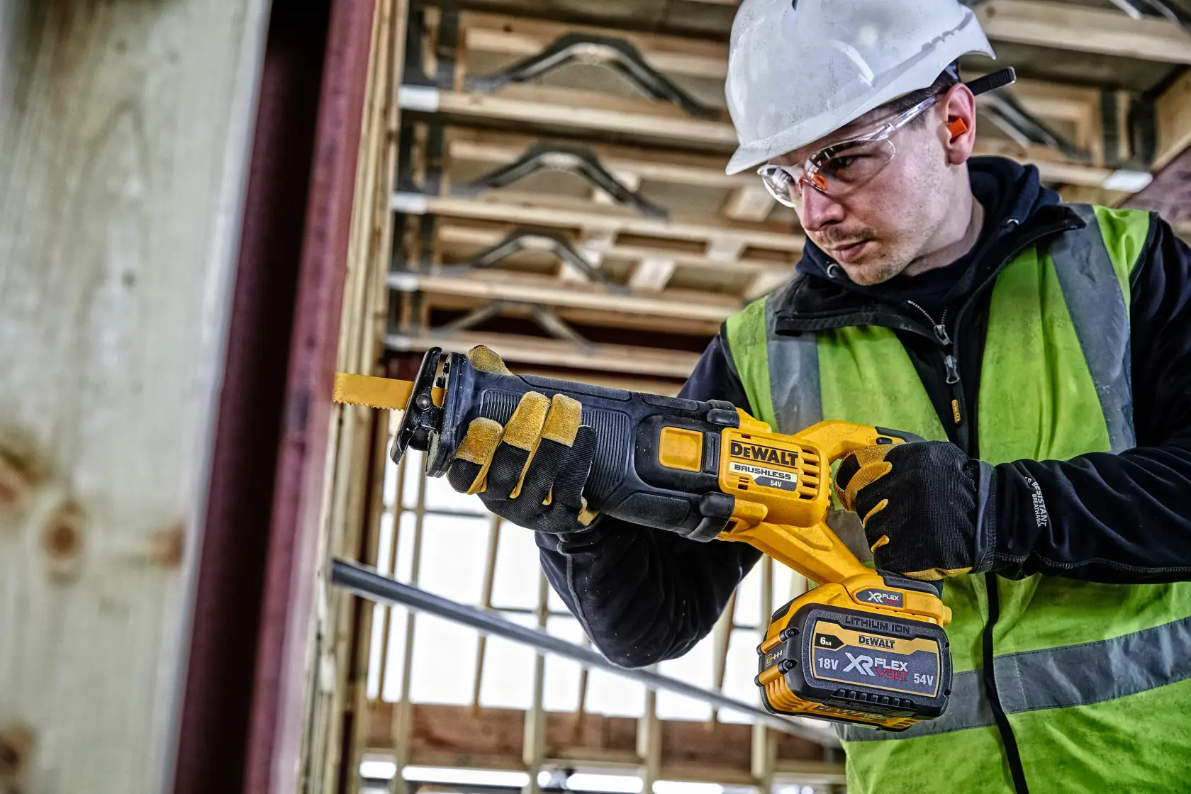 Worker using DEWALT DCS389T2 cordless saw at a construction site, wearing gloves, vest, and helmet.