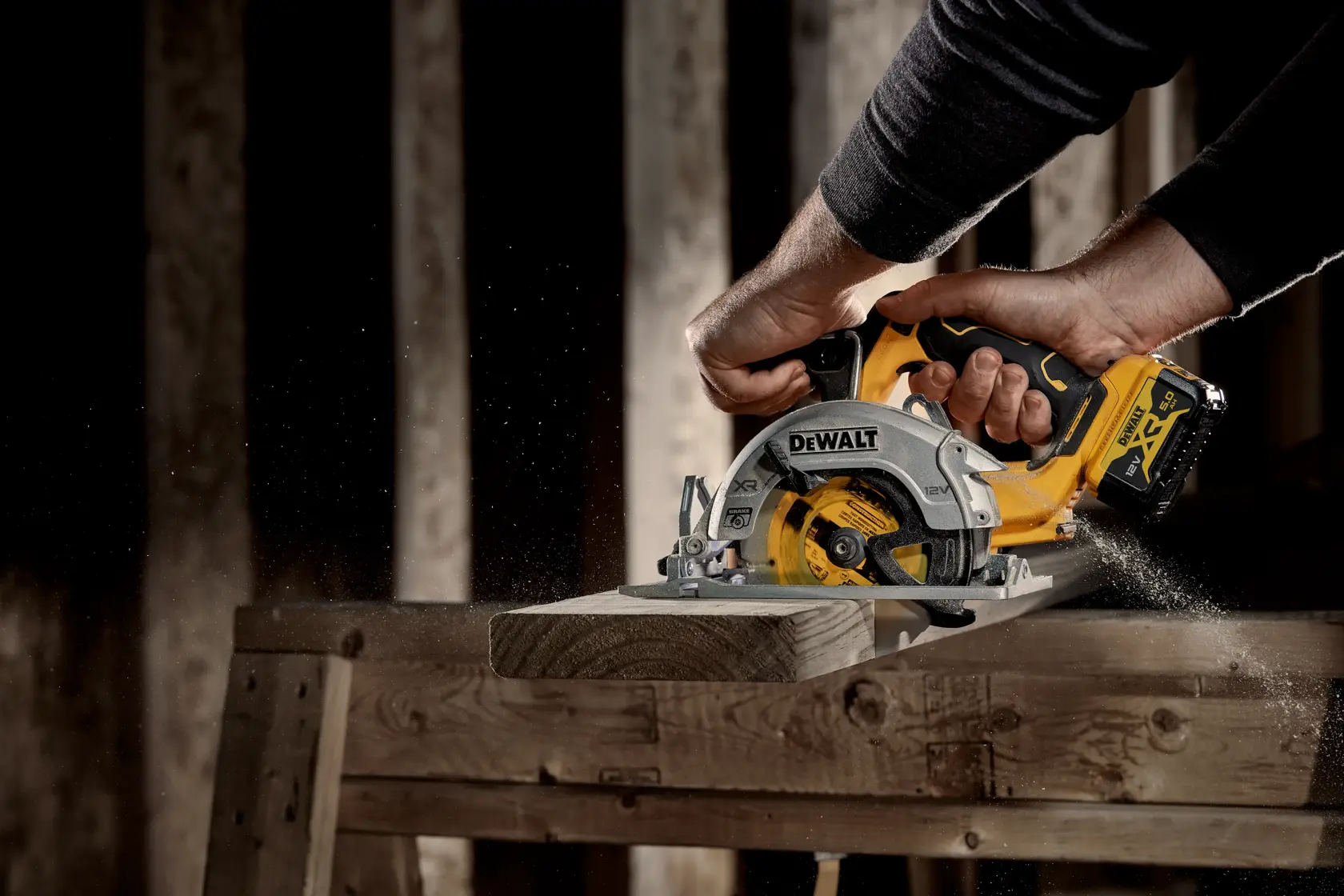 Person using a DEWALT cordless circular saw to cut wood on a workbench with sawdust flying.