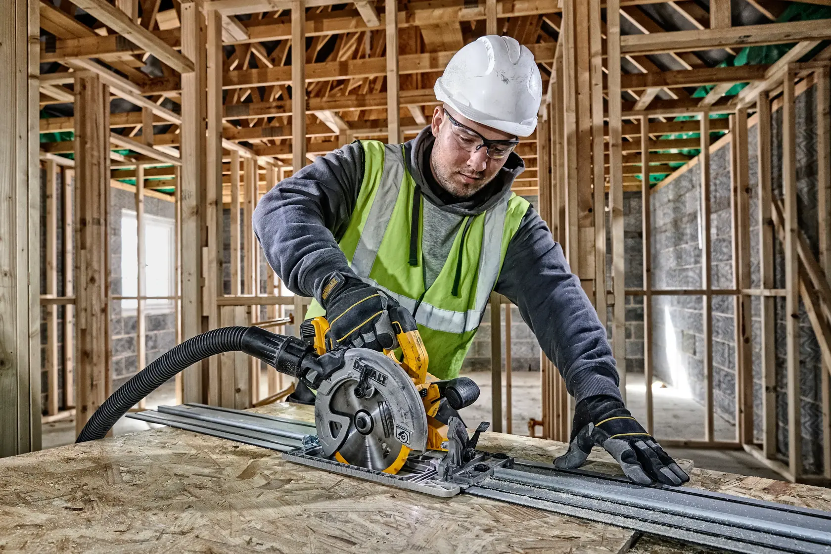 Worker uses a DEWALT circular saw with guide rail on wood inside a building under construction.