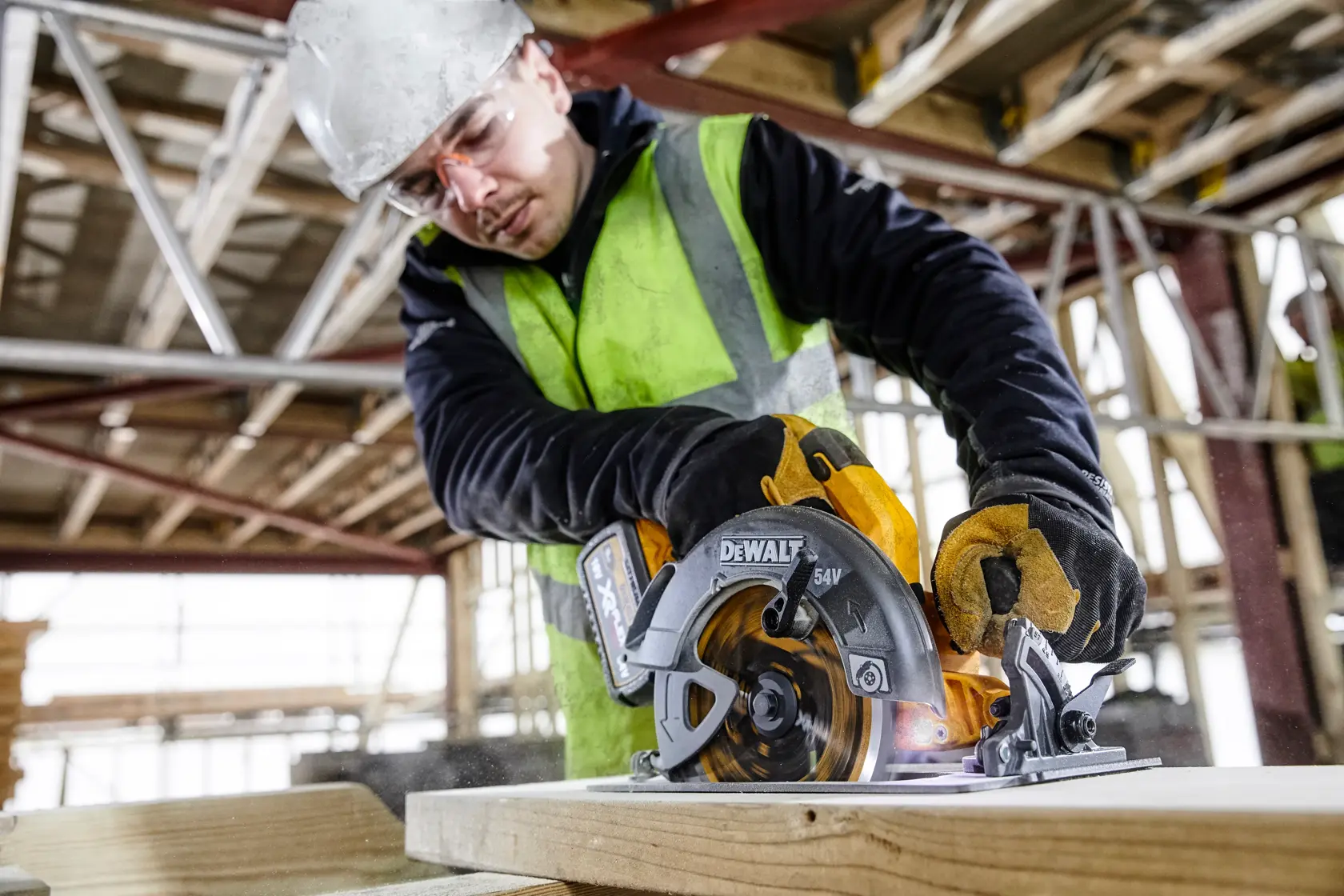 DEWALT DCS578NT circular saw cutting wood on a construction site, worker in safety gear.