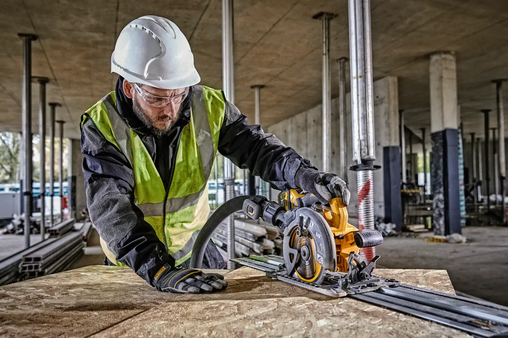Worker uses DEWALT circular saw DCS579NT on site, wearing safety gear and gloves.