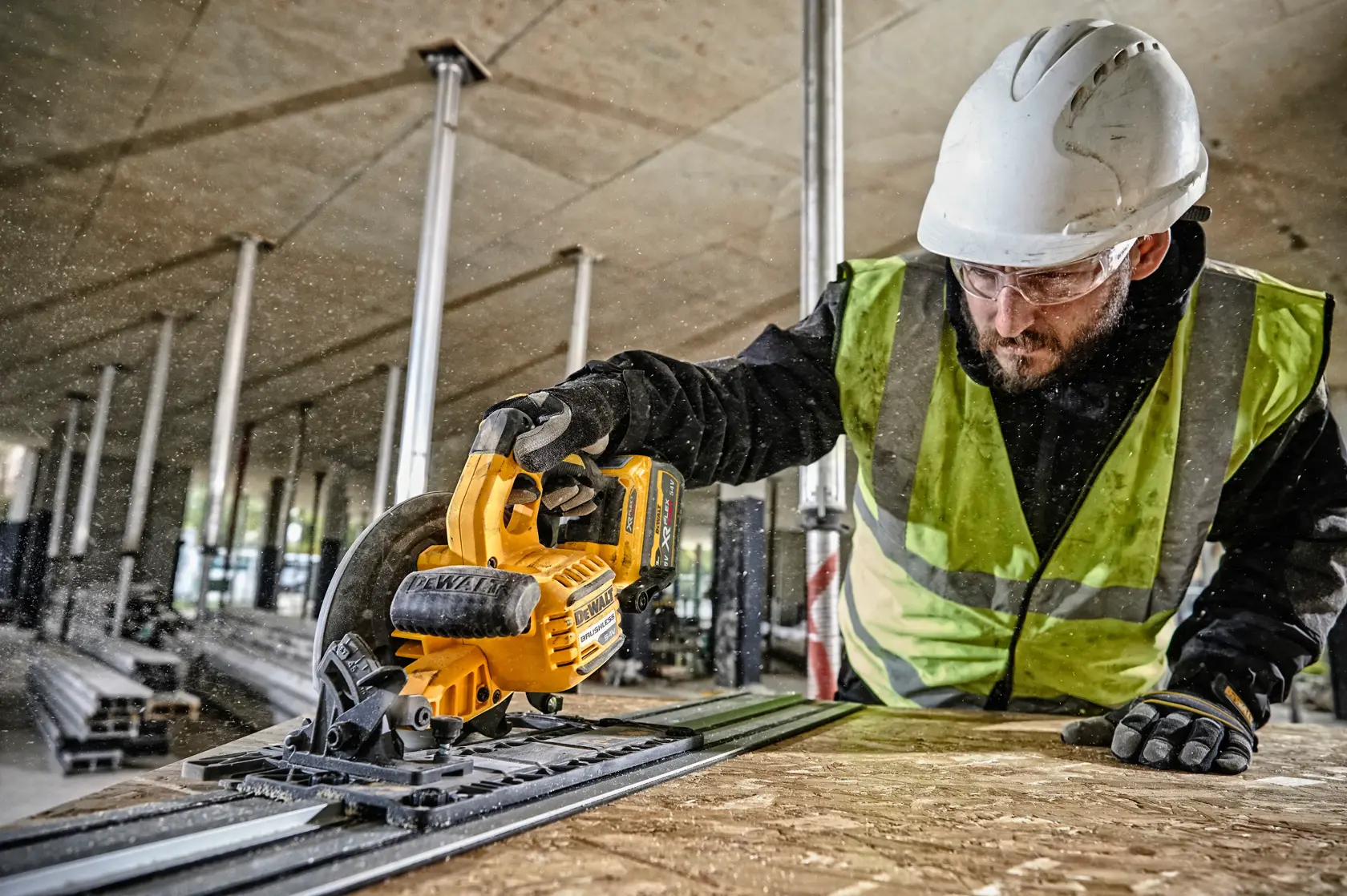 Worker uses DEWALT DCS579NT circular saw to cut wood at a construction site, wearing helmet and safety vest.