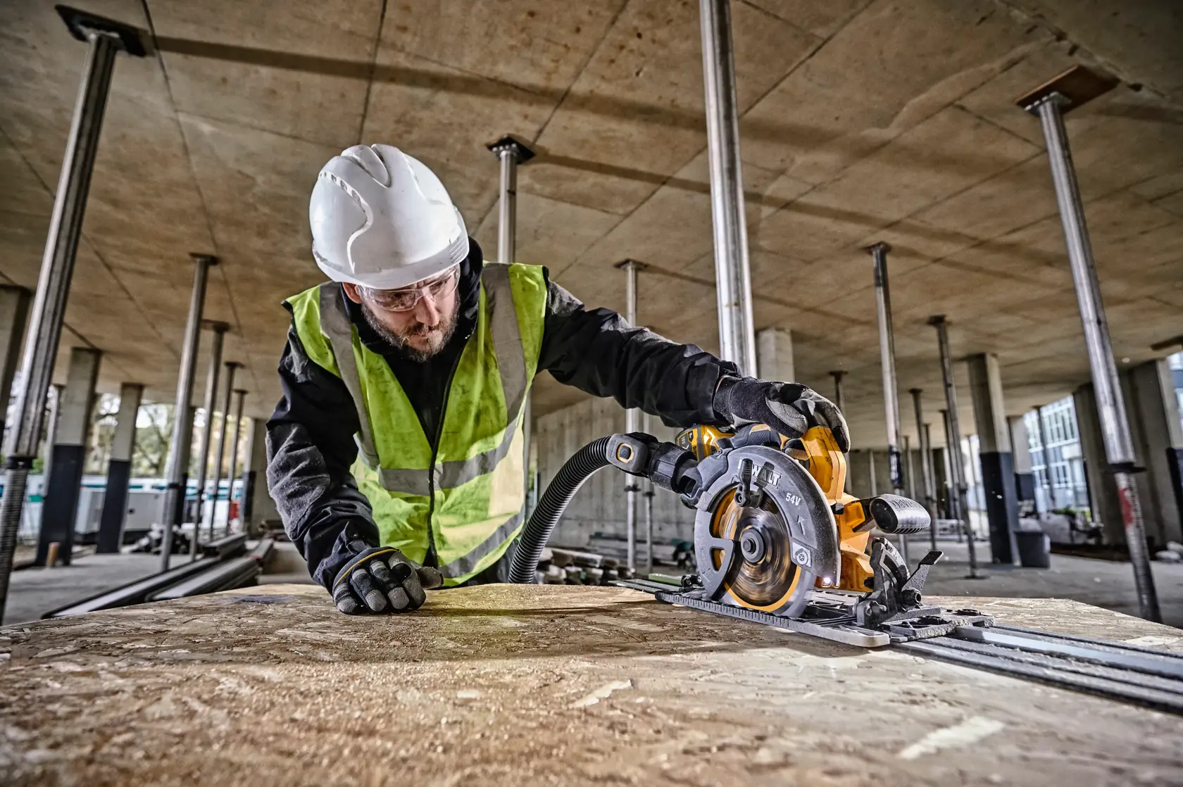 Worker cutting wood with a DEWALT DCS579NT circular saw at a construction site, wearing safety gear.