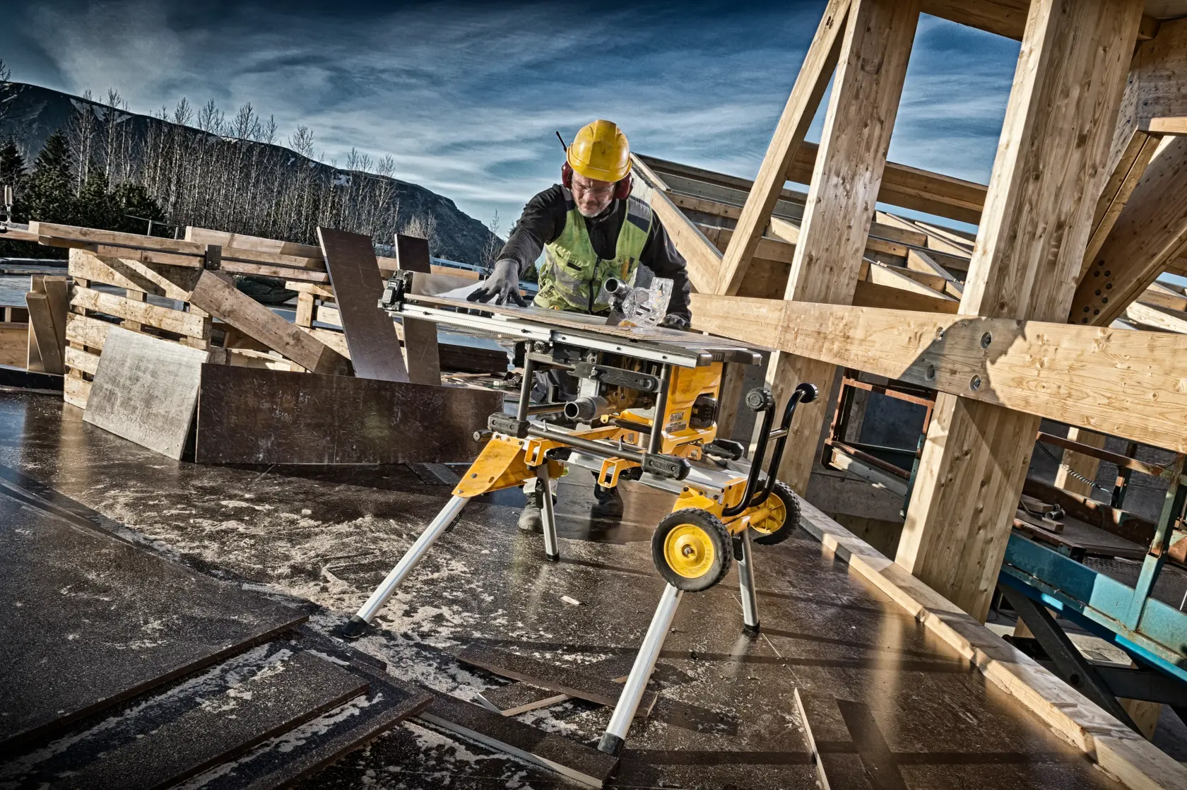 Worker uses DEWALT DCS7485N table saw on construction site with wooden beams and safety gear.