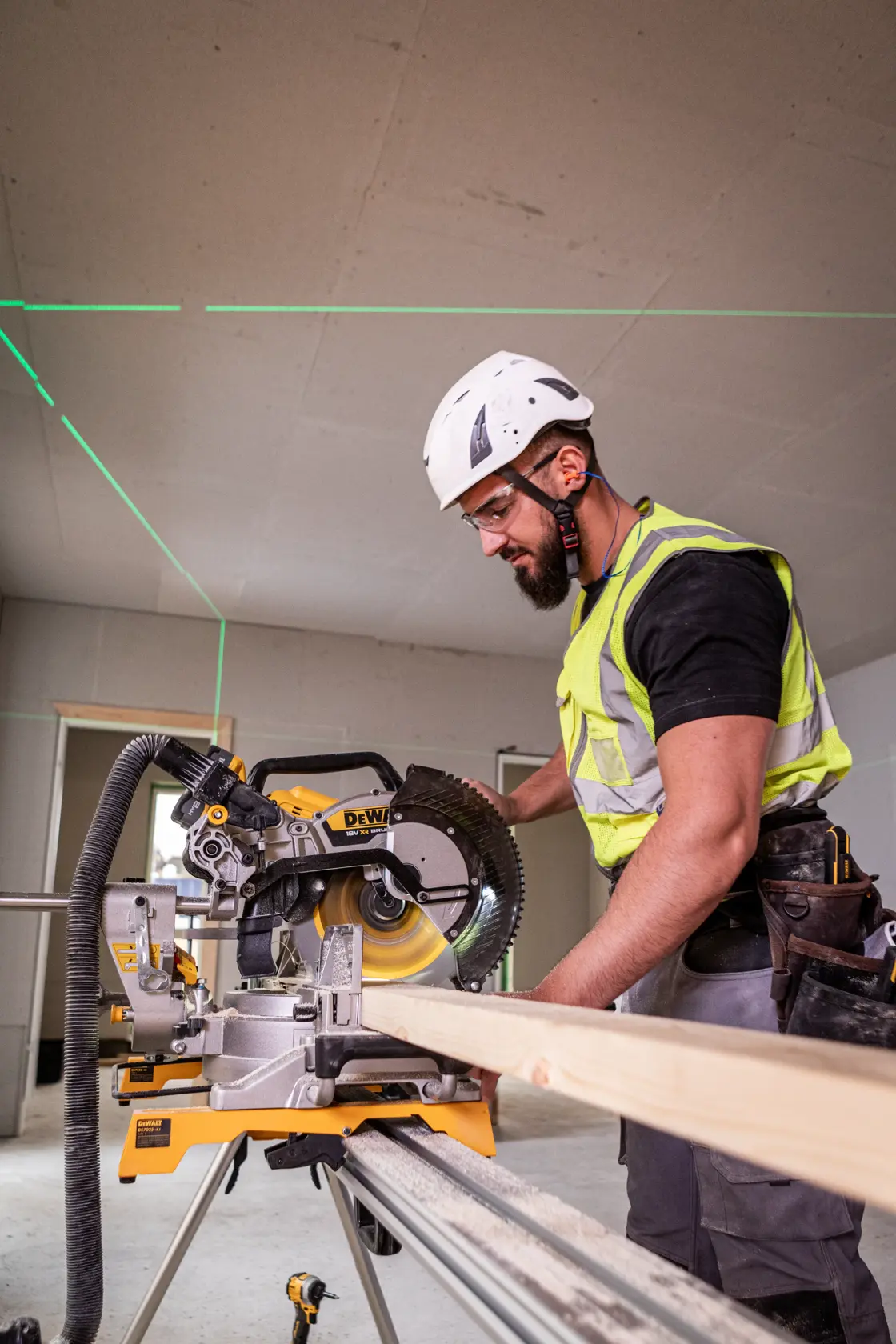 Worker using DEWALT DCS782N saw to cut wood indoors; safety gear and laser guides are visible.