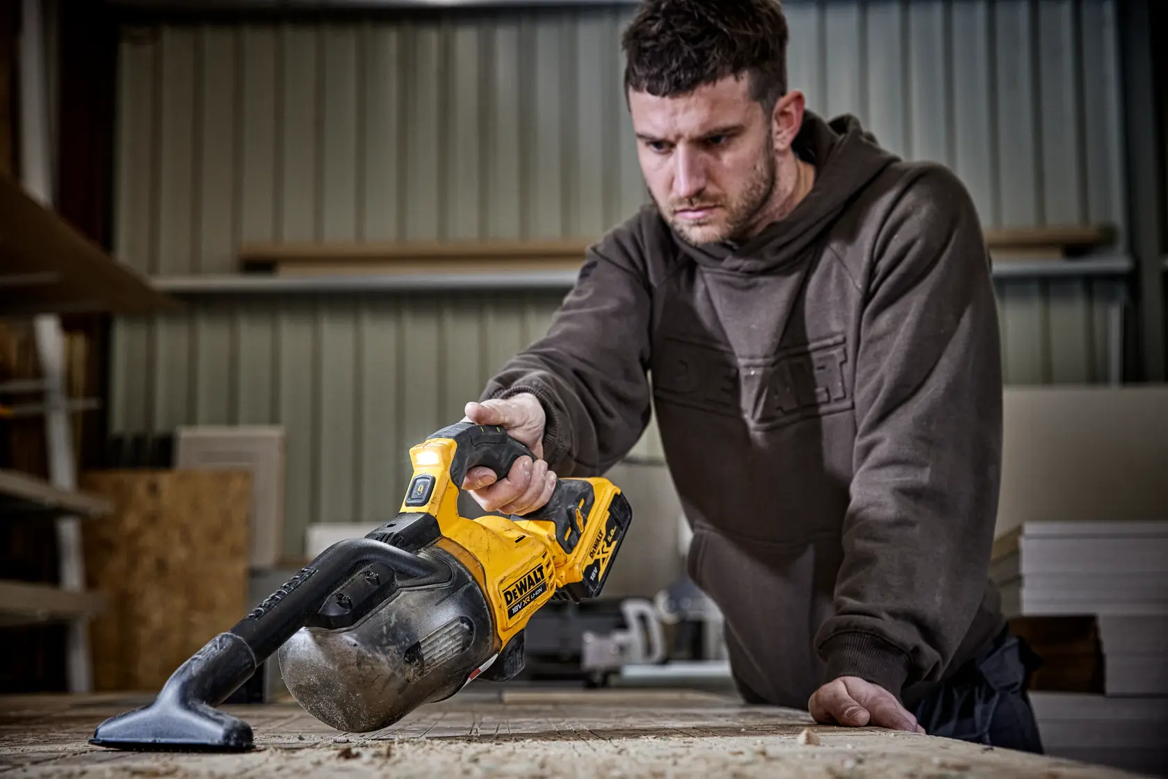 Person using a DEWALT DCV501LN cordless vacuum to clean a wooden workbench in a workshop.