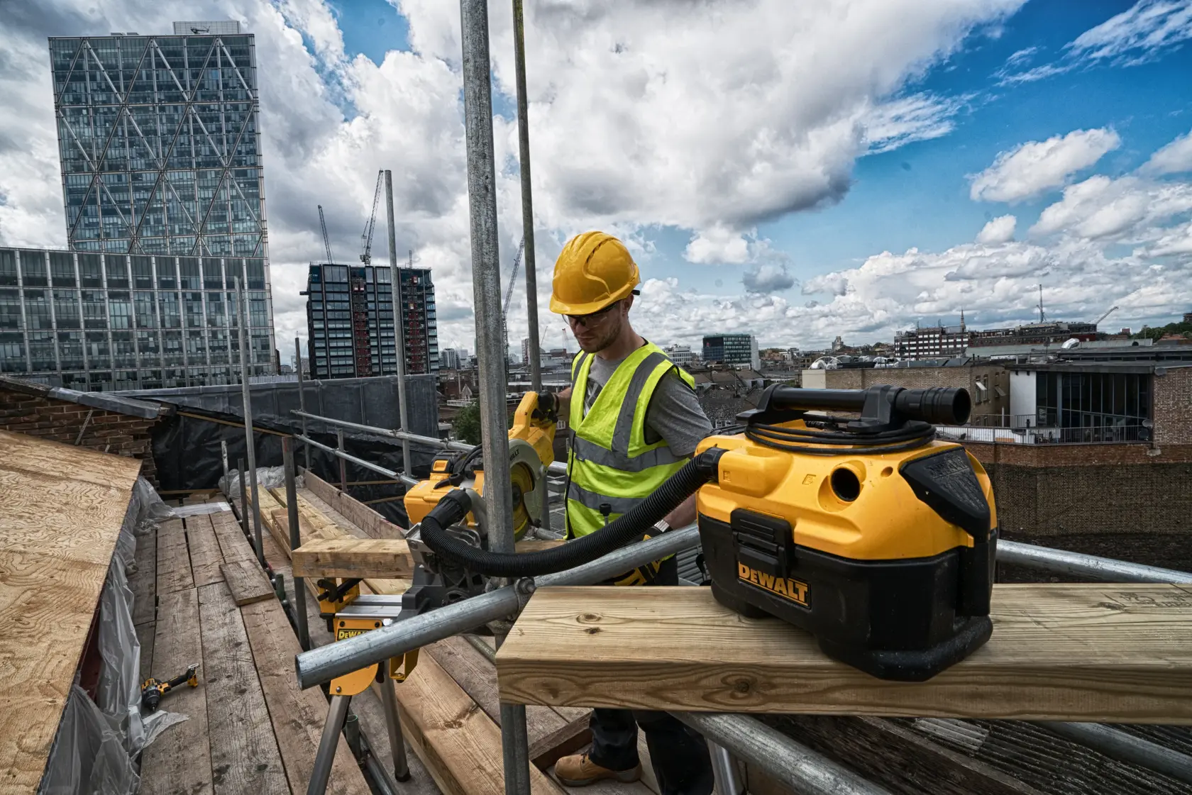 DEWALT DCV584L vacuum used by a worker on a construction site with city buildings and cranes in the background.