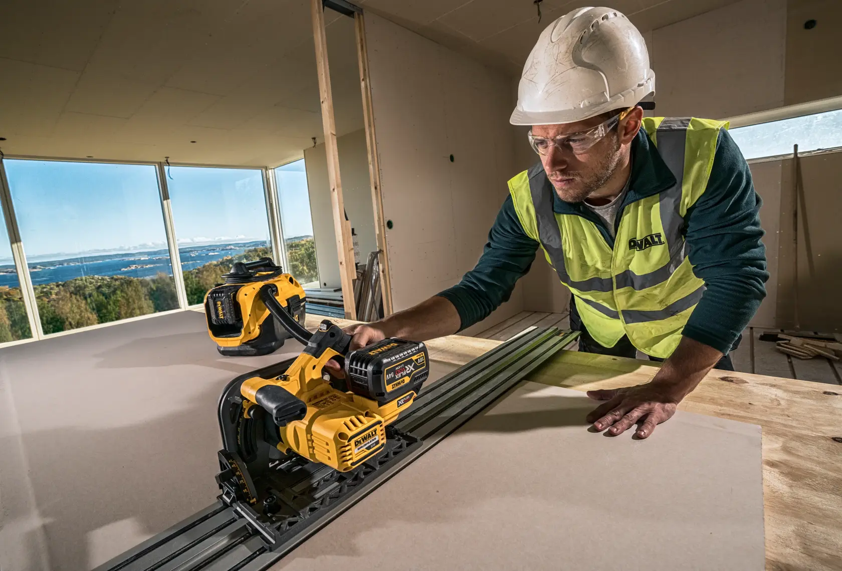 Worker uses a DEWALT cordless saw on a construction site, wearing a helmet and safety vest.