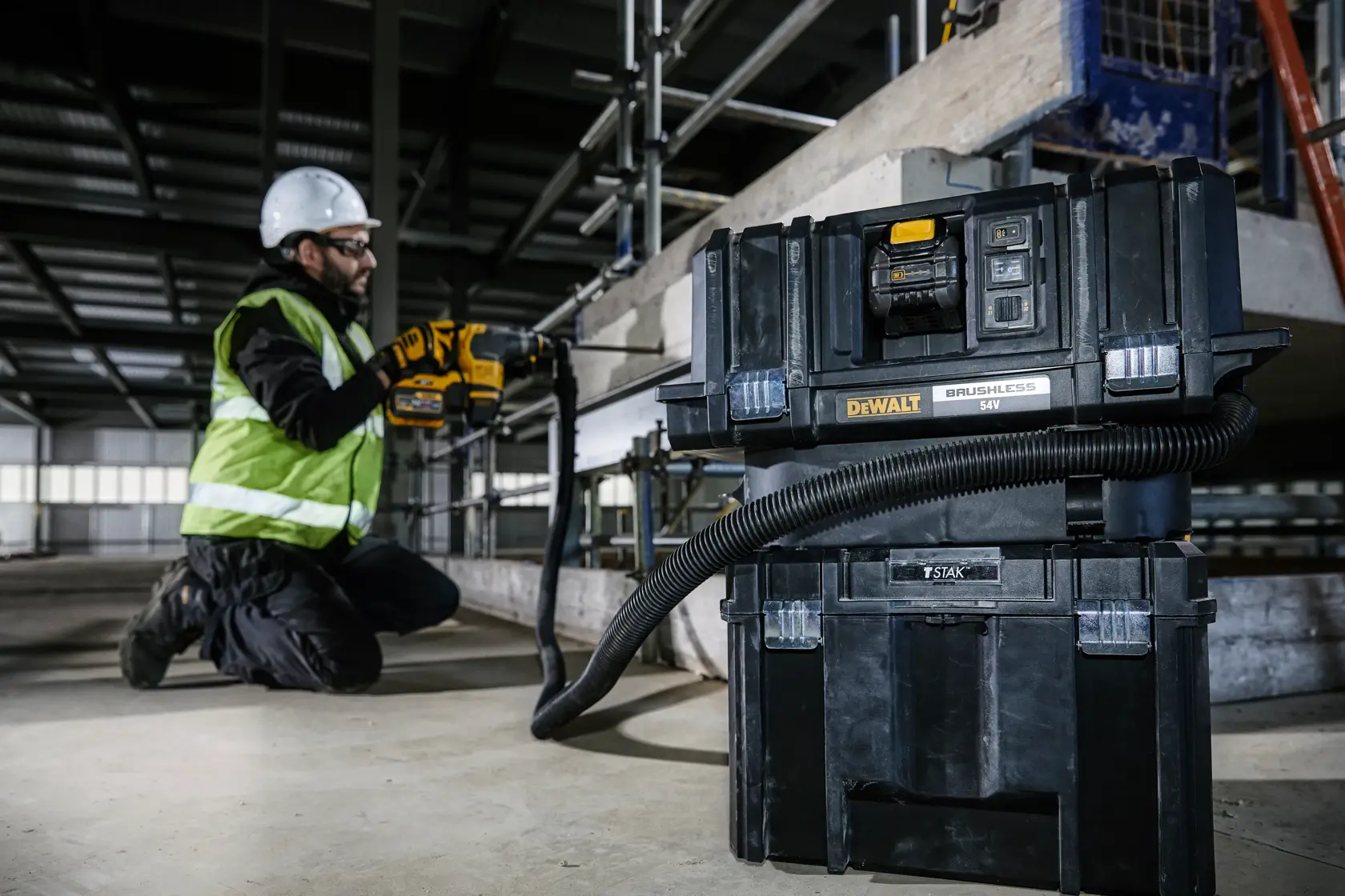 DEWALT DCV586MT2 vacuum in use on a construction site, connected to a tool operated by a worker with safety gear.