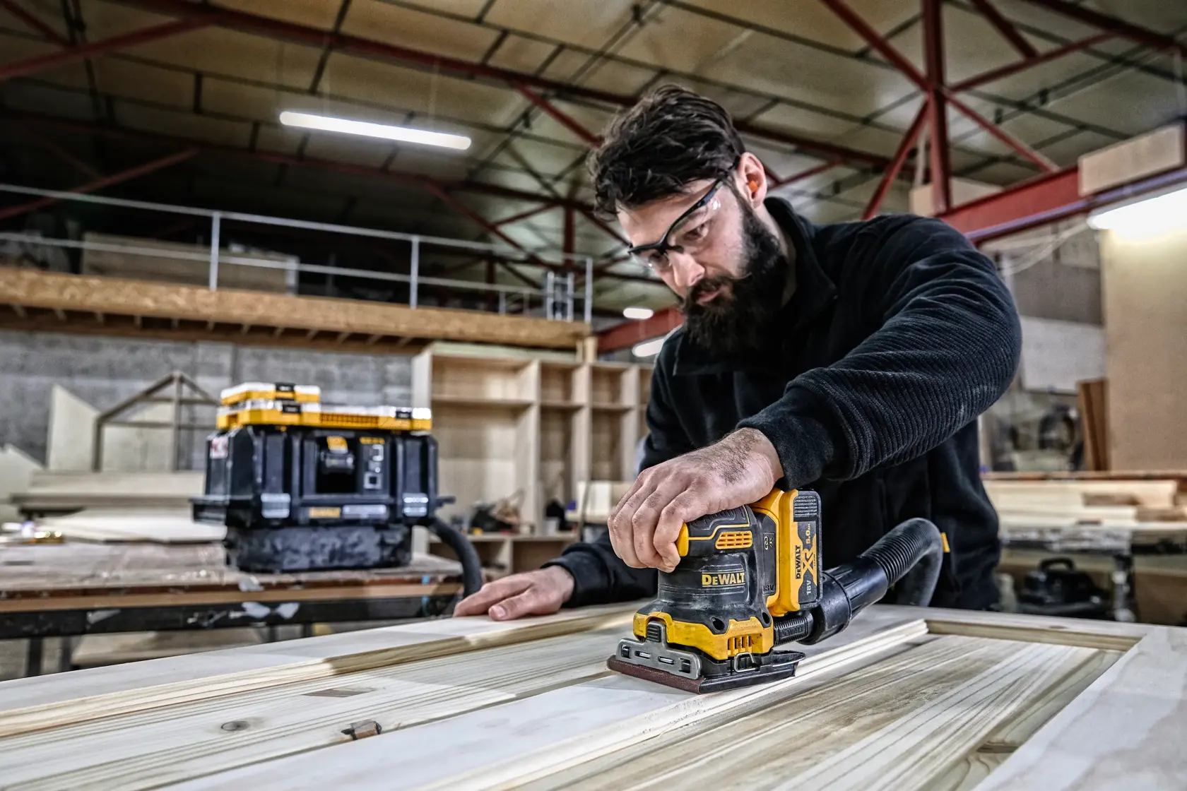 Person using a DEWALT DCW200N sander on wood in a workshop. Tool box visible in background.
