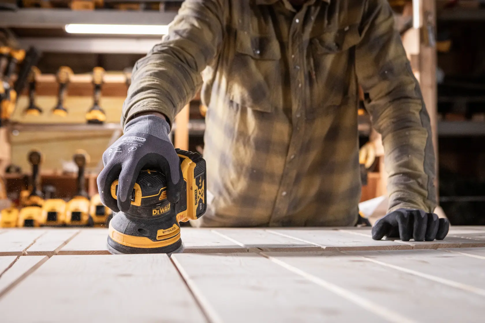 Person sanding wood with a DEWALT DCW200N cordless sander in a workshop.