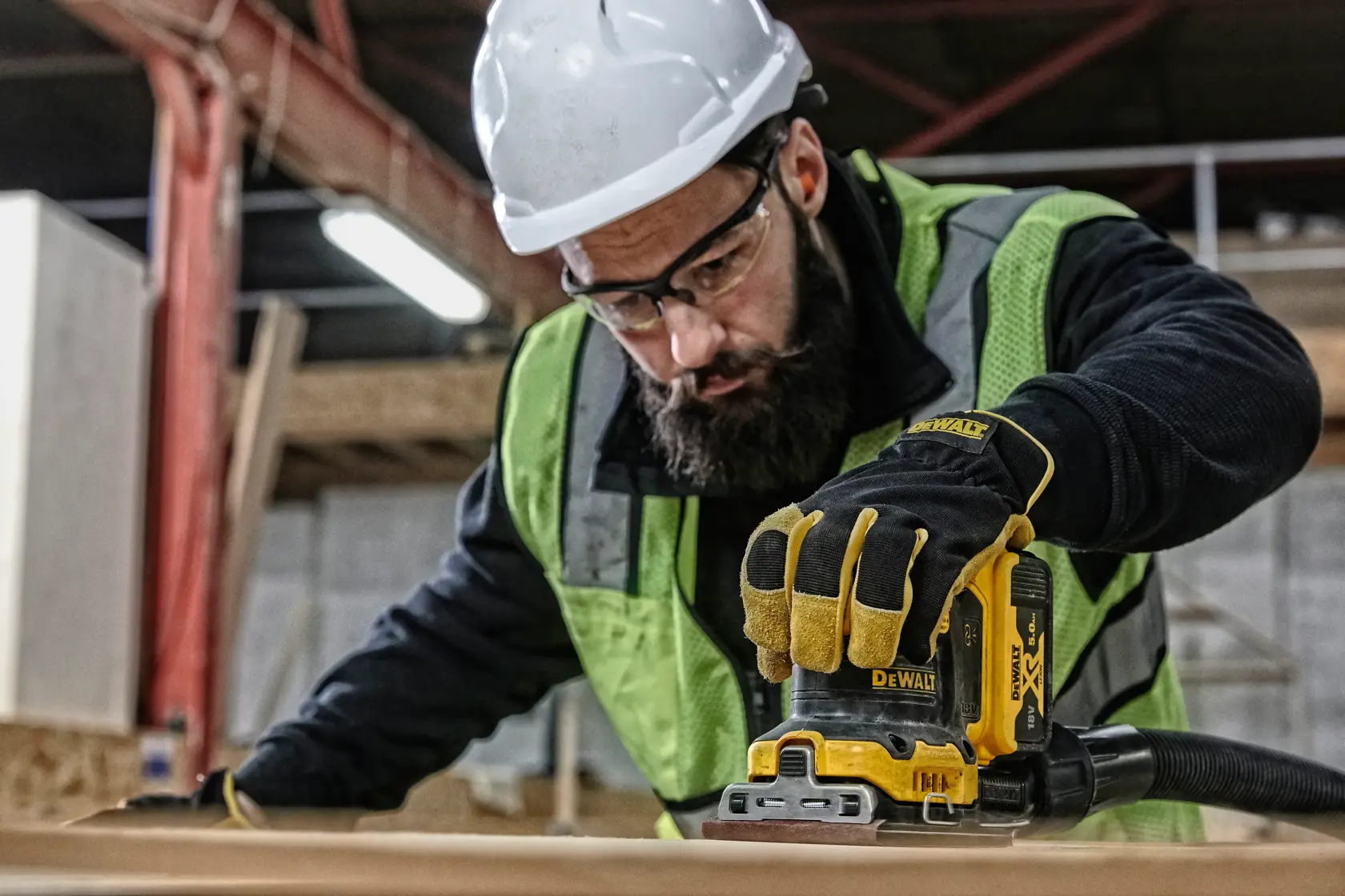 Operaio usa DEWALT DCW200P2 su legno, con guanti, casco e gilet di sicurezza in cantiere.