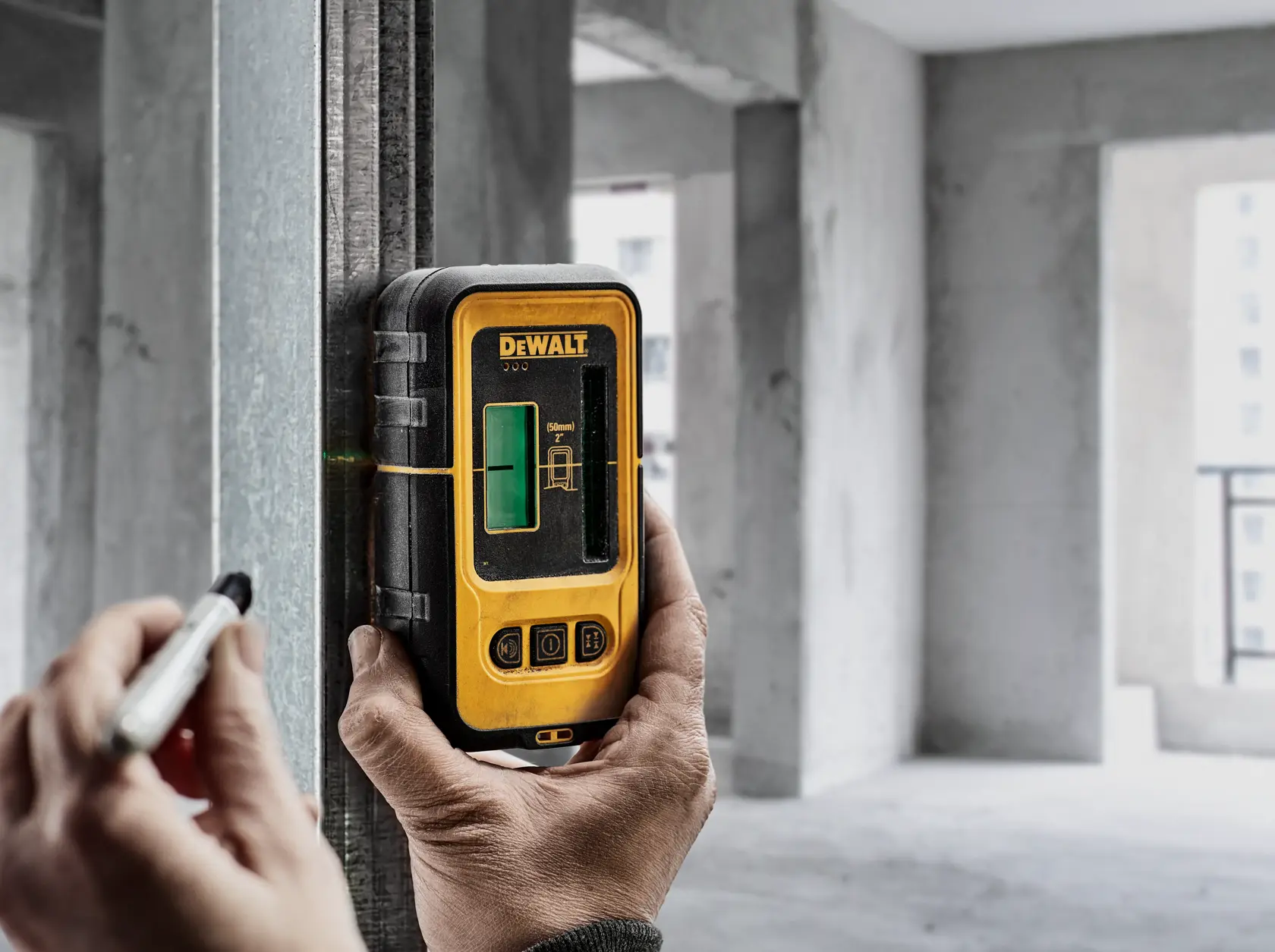 Person uses DEWALT laser detector DE0892G on a metal beam in an unfinished building interior.