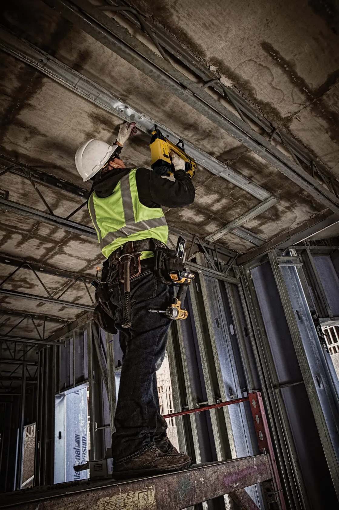 Worker using DEWALT DGN845D1-QW, DGN845D1 tool on ceiling at construction site. Photography category.