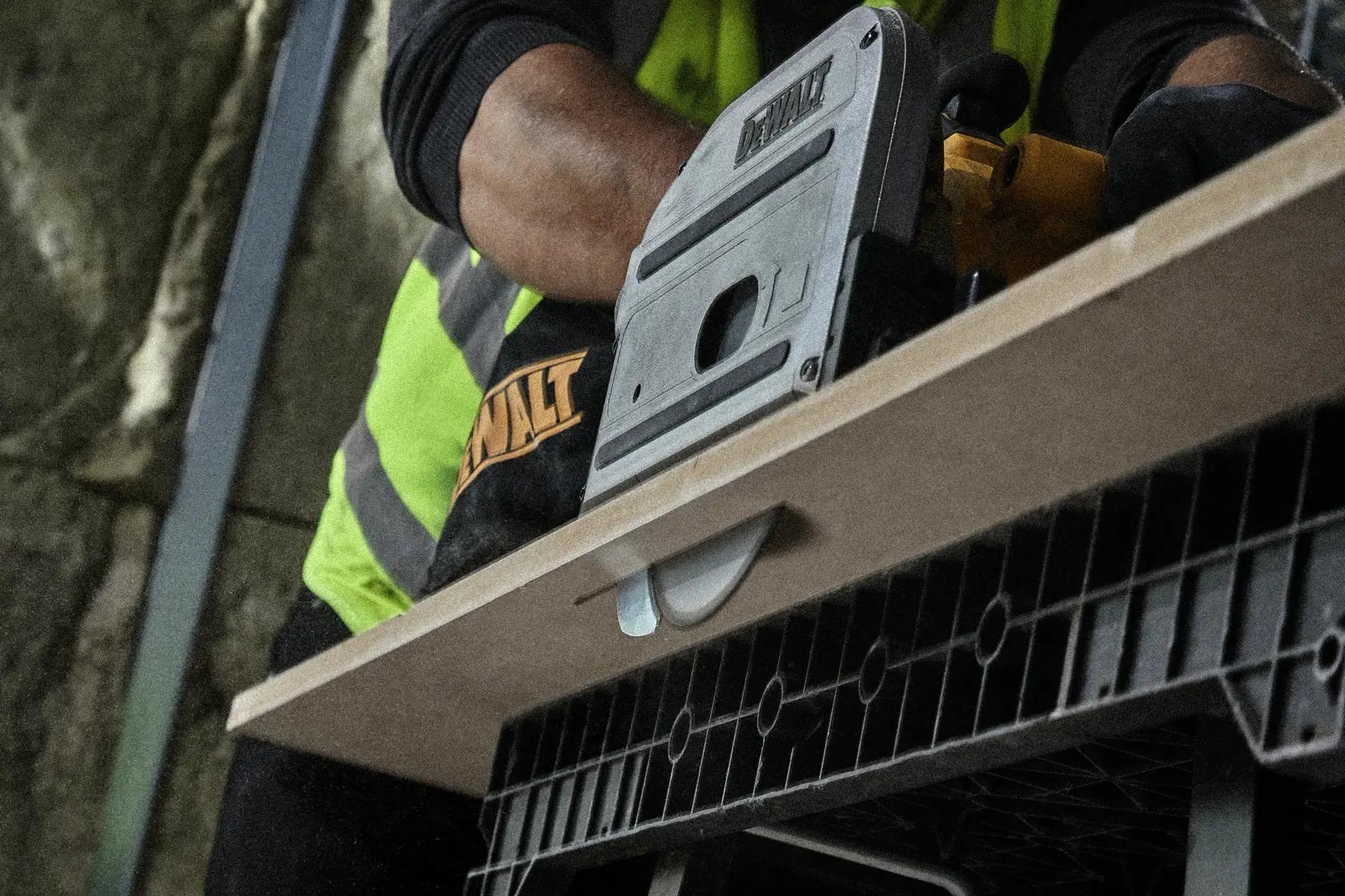 Person using a DEWALT saw to cut wood on a workbench. Close-up view, focus on tool and wood.