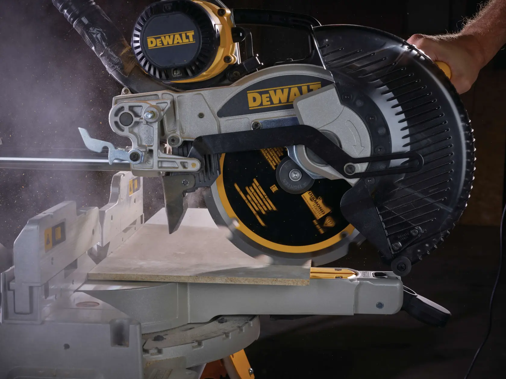Una troncatrice DEWALT taglia una tavola, polvere e movimento visibili durante l’uso.