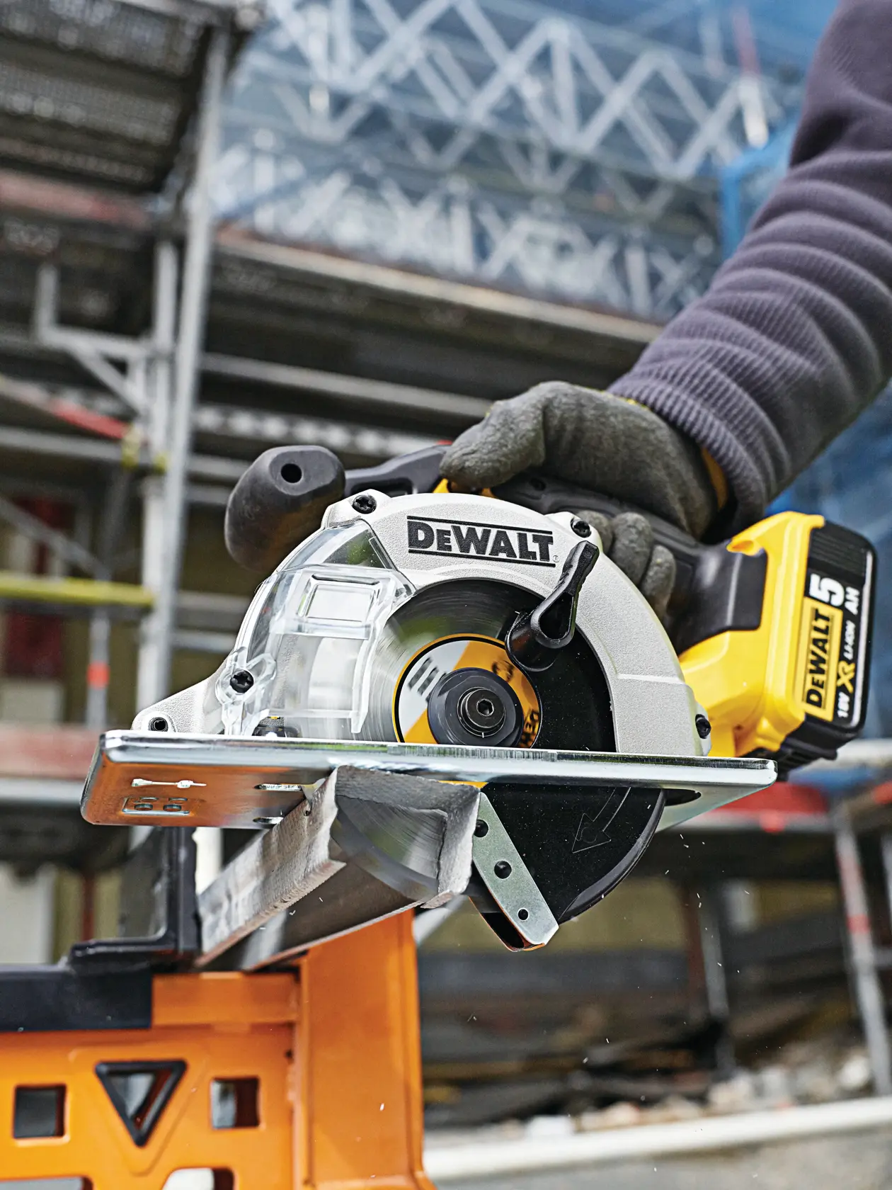 DEWALT cordless circular saw cutting metal at a construction site, operated by a person wearing gloves.