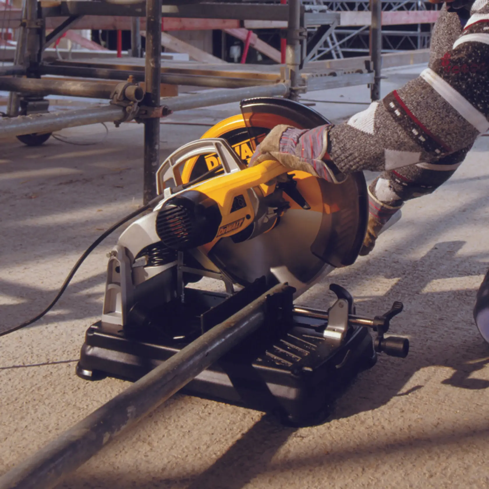 Worker uses DEWALT DT1922 saw to cut metal pipe at construction site, wearing gloves for safety.