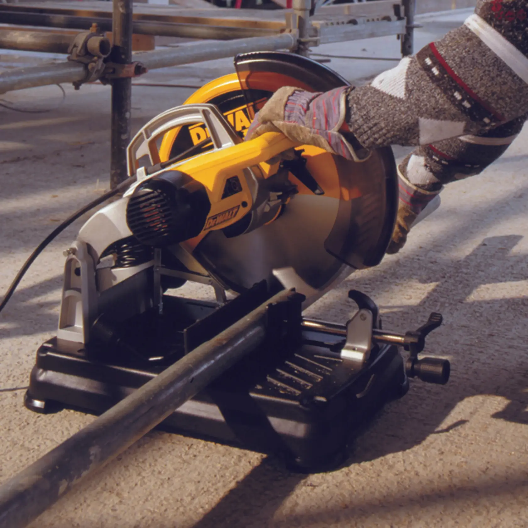 Person uses DEWALT DT1927 power saw to cut metal pipe outdoors. Safety gloves are worn.