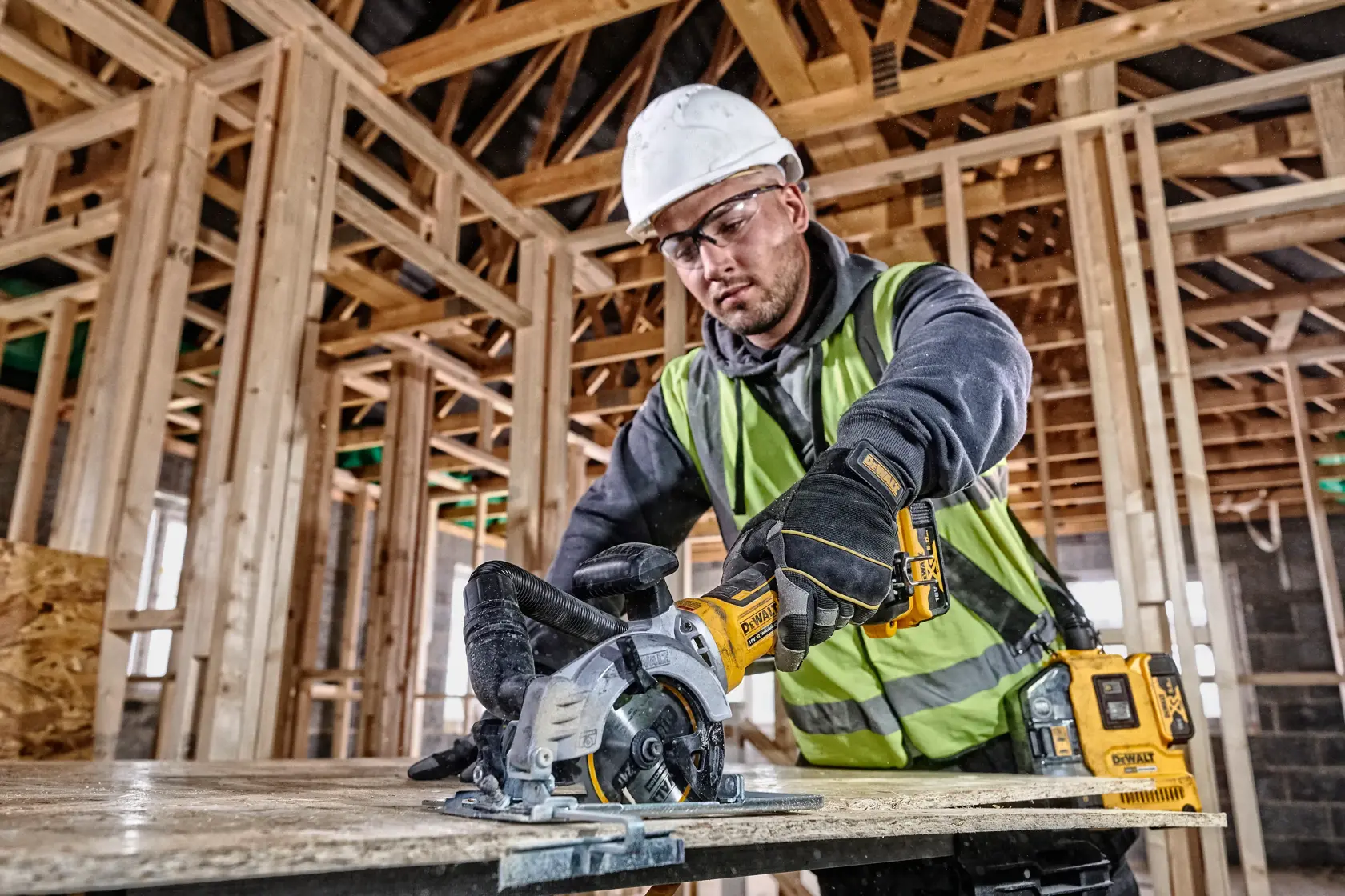 Operaio usa sega circolare DEWALT su legno in cantiere, con giubbotto riflettente e casco.