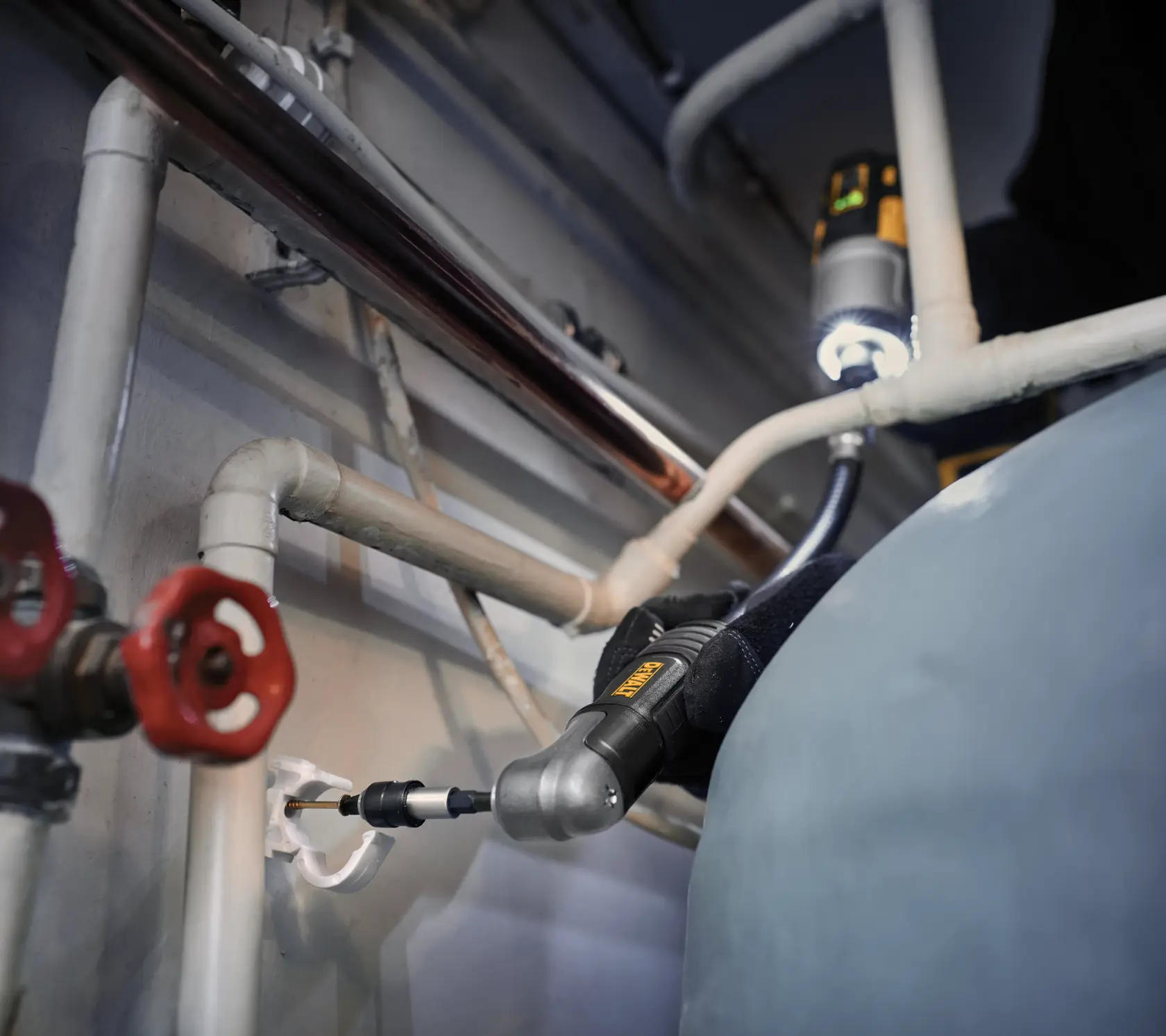 DEWALT right angle drill being used to drill near pipes in a confined workspace.