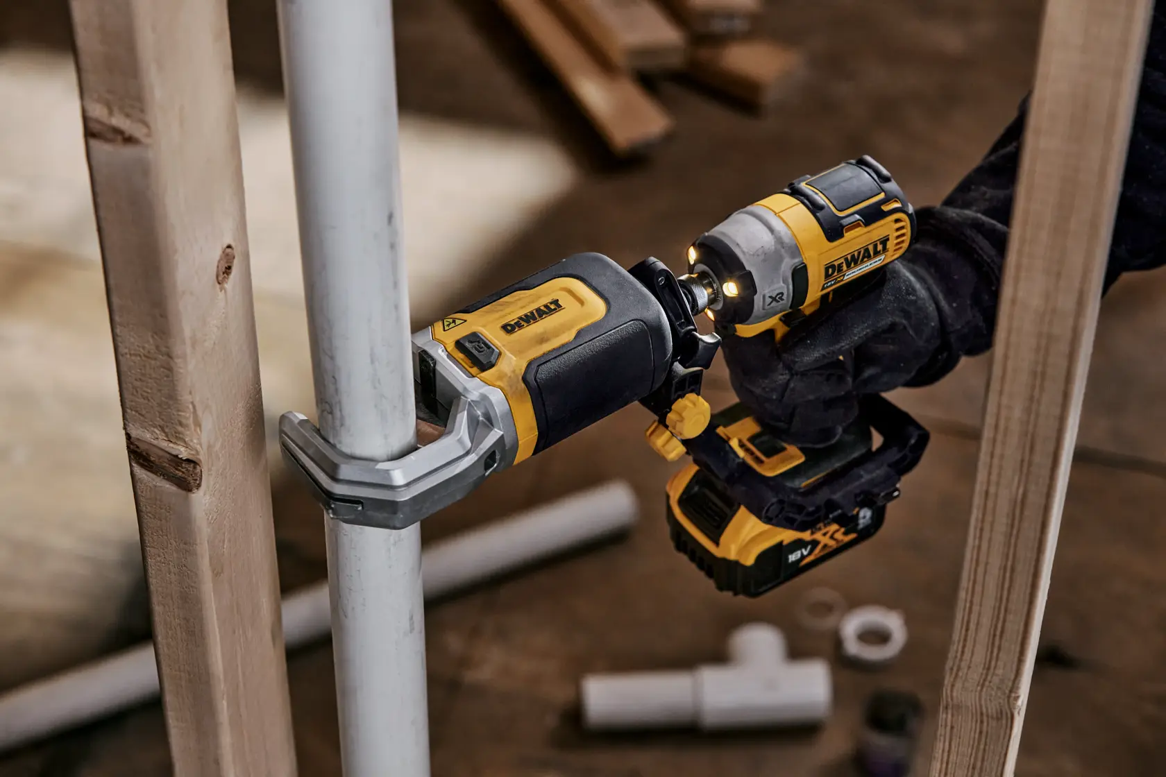 Et DEWALT DT20560 elektroverktøy brukes til å feste en klemme på et metallrør, holdt av en person med hanske. Verktøyet er gult og svart, med andre rør og trebord i bakgrunnen.