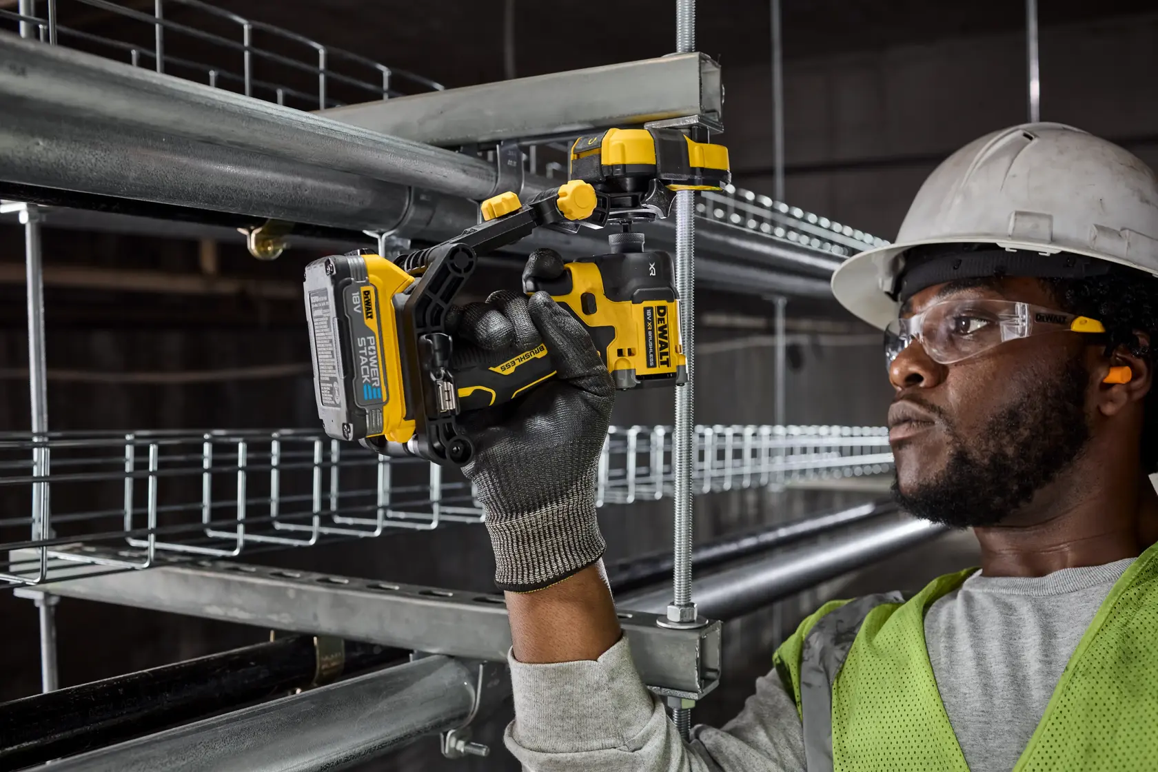 Worker uses DEWALT cordless drill to install metal conduit, wearing gloves, safety vest, and helmet.
