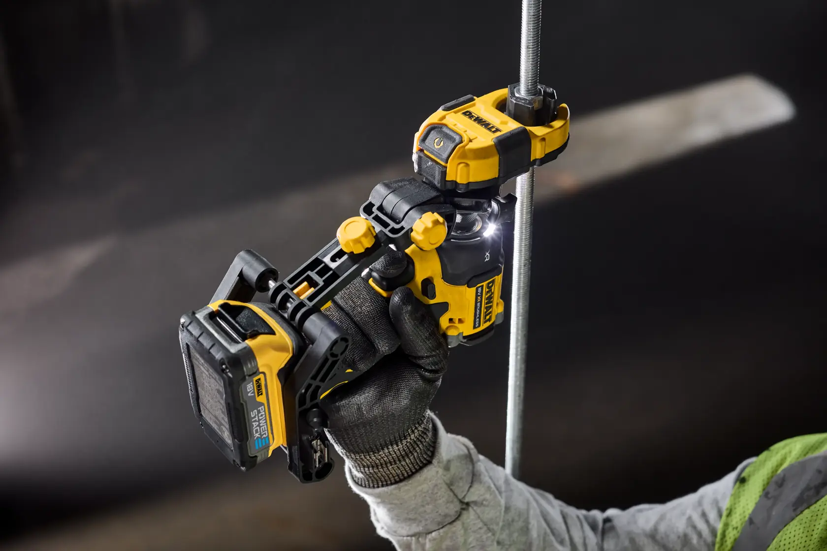 A DEWALT power tool is held by a gloved hand, cutting a metal rod in a dark industrial setting.