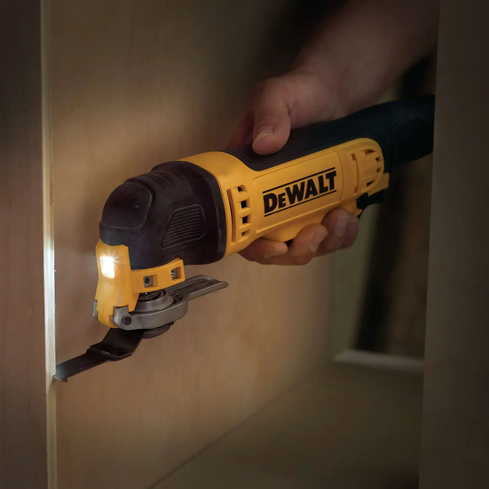 DEWALT multitool used for precise cutting in wood, held by a hand. Tool features LED light.
