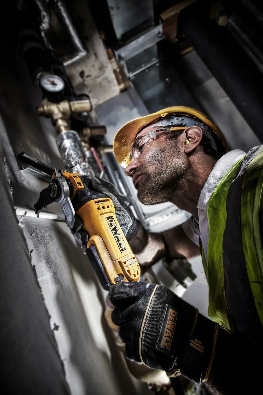 Worker using a DEWALT DT20701 power tool for cutting metal pipes, wearing safety gear in an industrial setting.