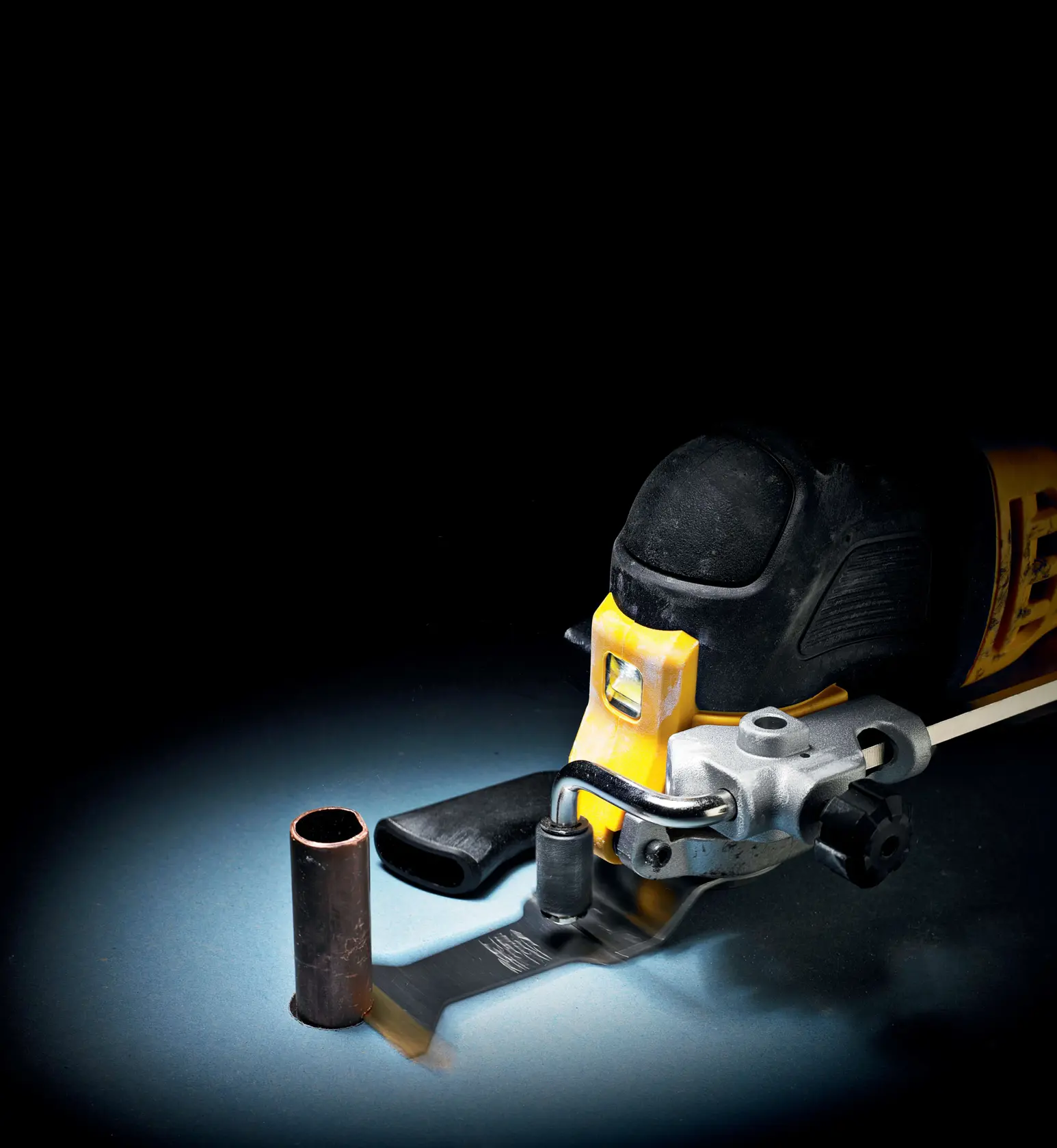 DEWALT oscillating tool cutting a metal pipe. Tool and pipe are on a dark background.