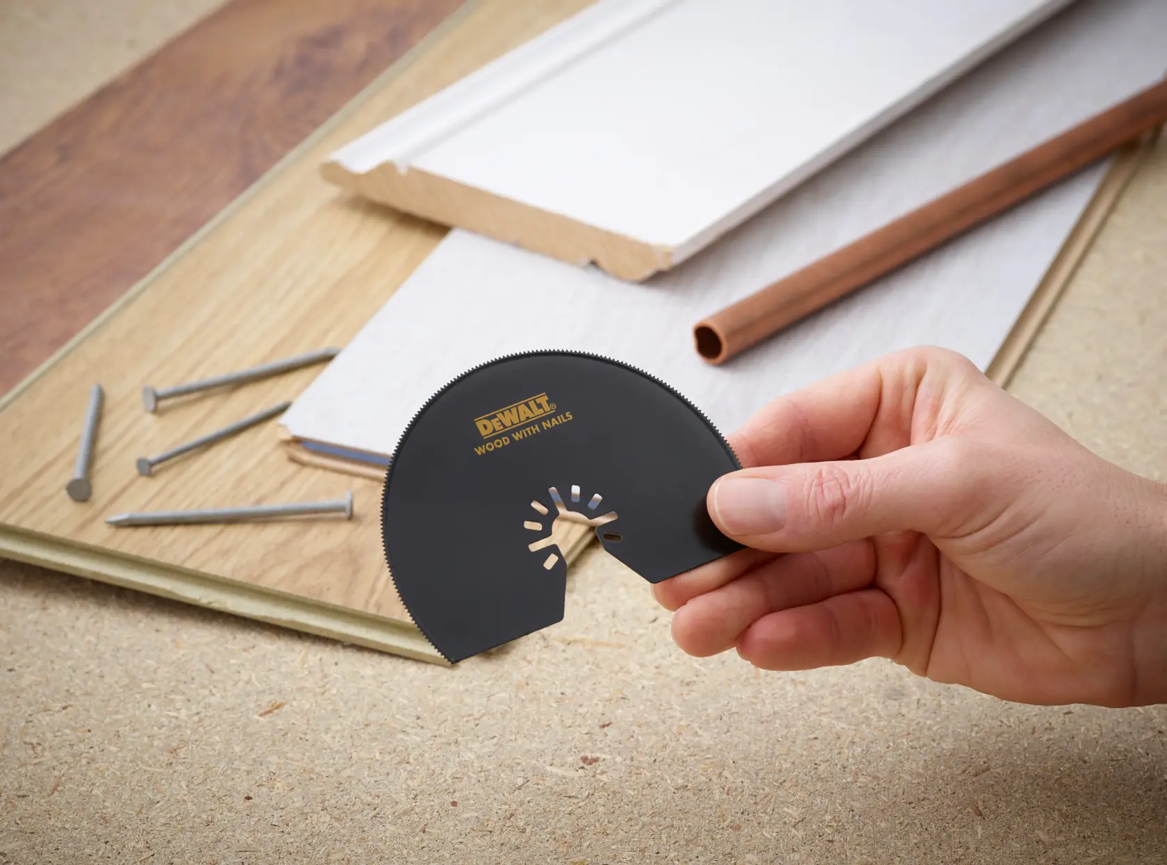 Hand holding DEWALT DT20708 saw blade, with wood, nails, and pipe in background.